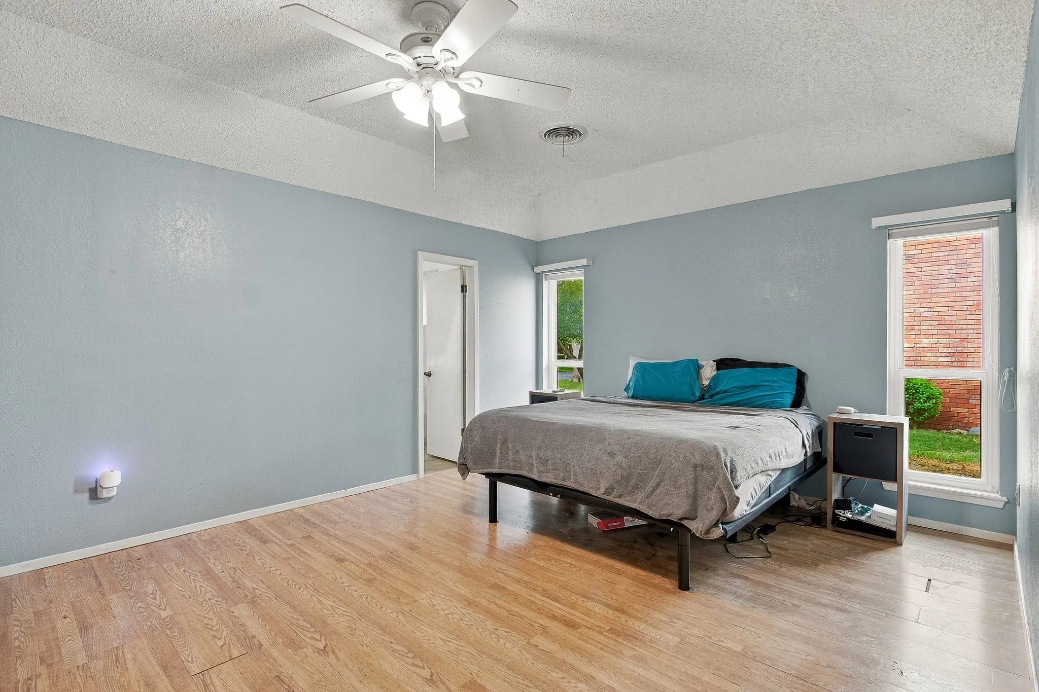 Wood-finish flooring, vaulted ceiling, white ceiling fan with integrated lighting, multiple windows, and a solid core door