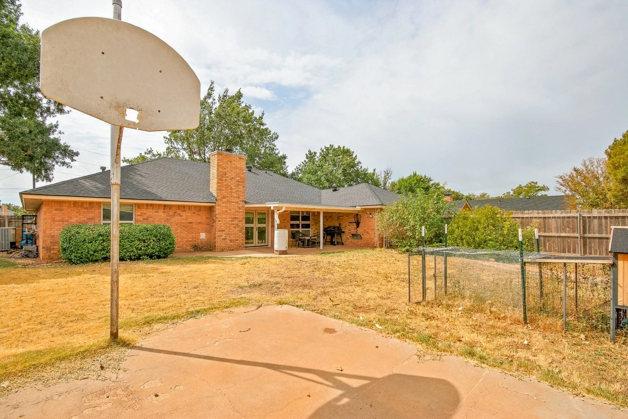 Brick exterior with a covered patio, a concrete patio, and a wood privacy fence