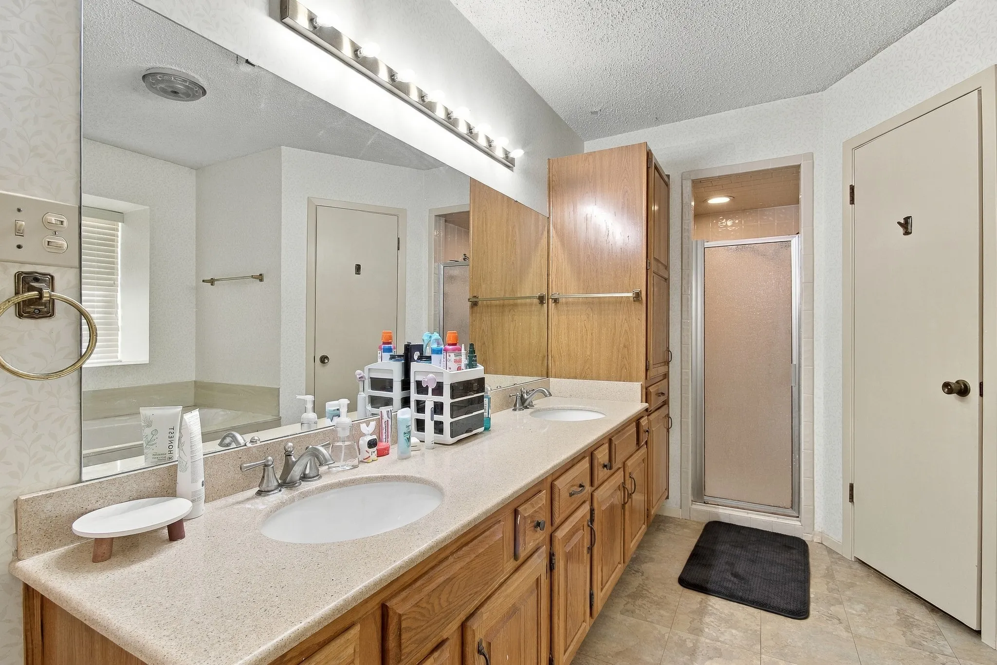 Double vanity with integrated sinks, wood-finish cabinetry, built-in storage tower, and a glass-enclosed shower