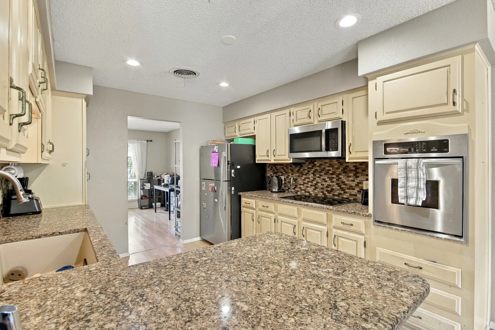 Cream-finish cabinetry with decorative hardware, stainless steel built-in oven, integrated cooktop, and a mosaic tile backsplash