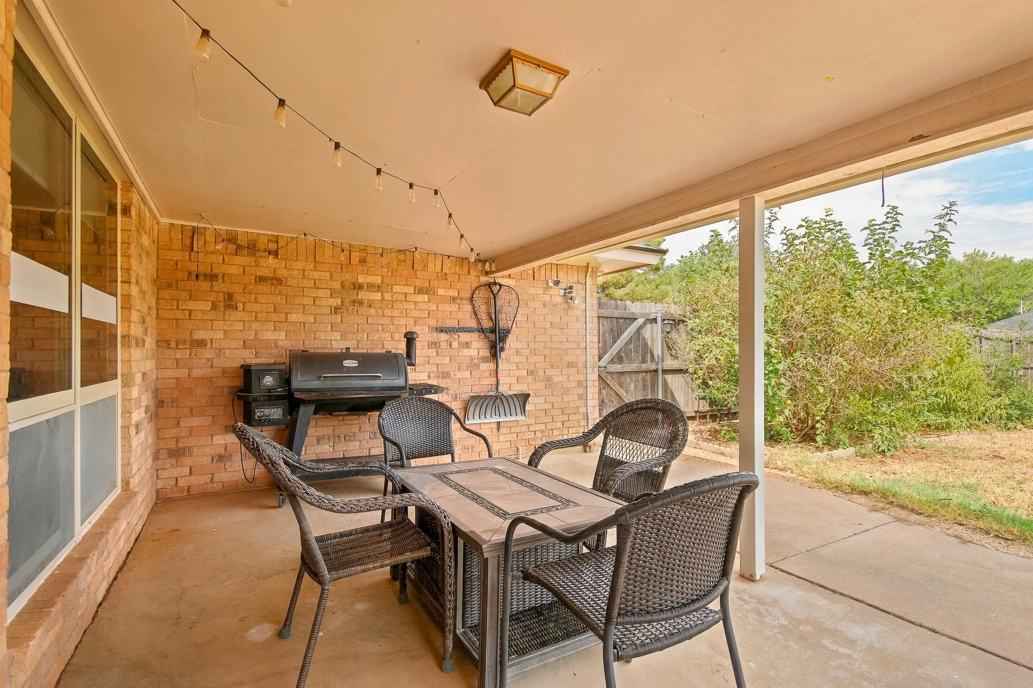 Covered patio featuring a brick wall, concrete flooring, and an overhead light fixture