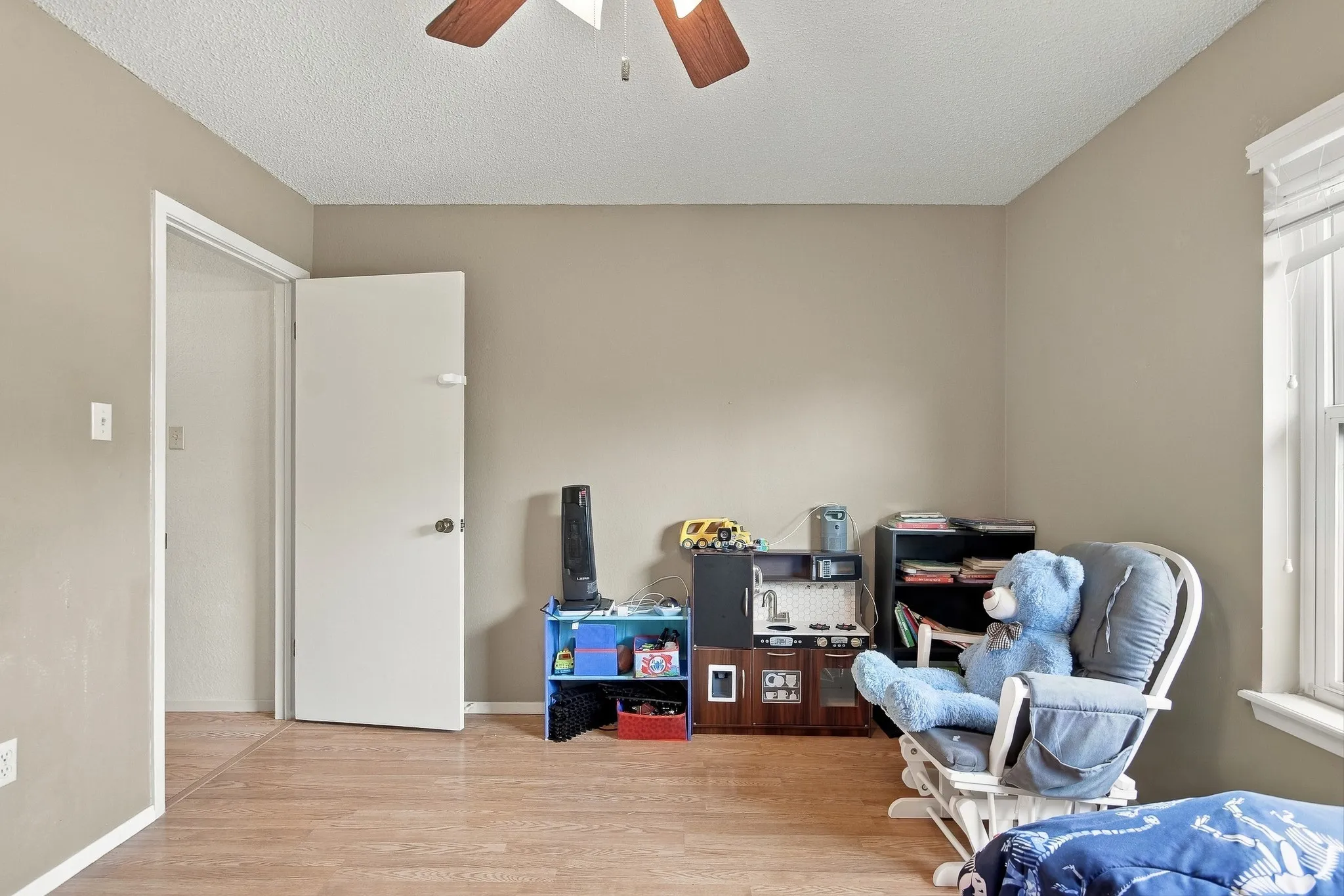 Wood-finish flooring with neutral wall paint, a ceiling fan, and window with blinds