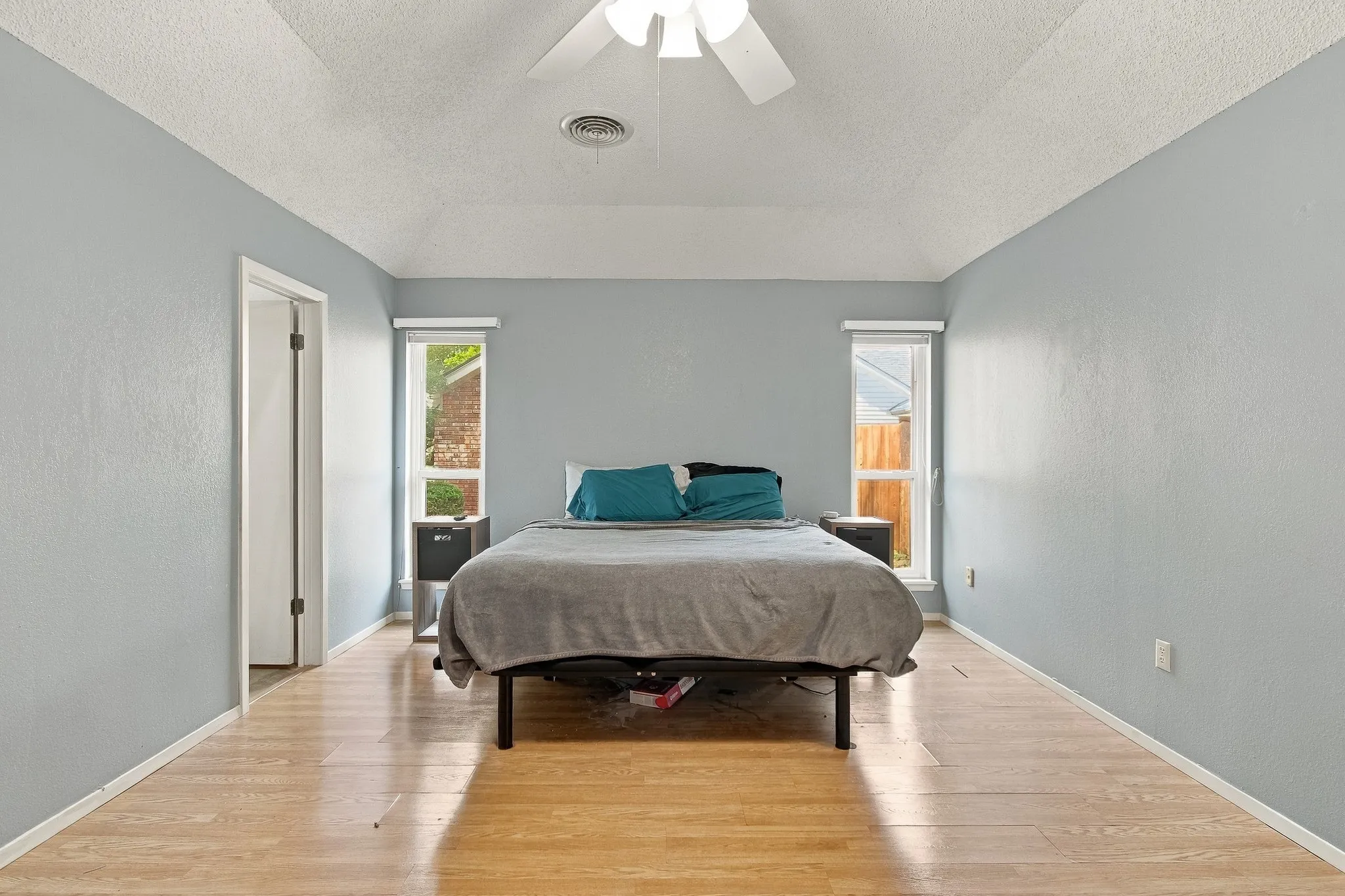 Vaulted ceiling, ceiling fan, two windows, light wood-finish flooring, and a neutral wall color