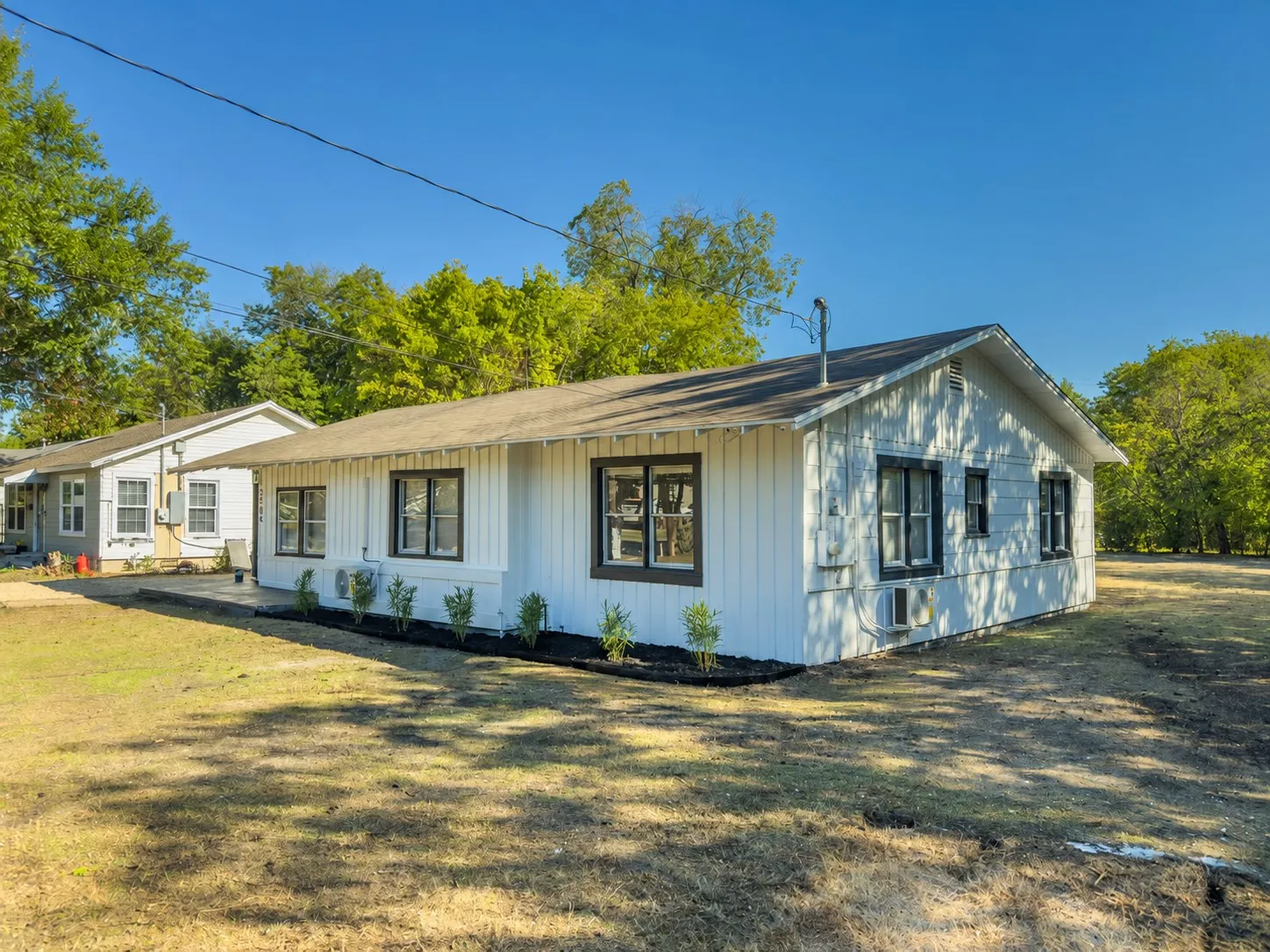 White exterior siding with dark trim windows, front landscaping with dark mulch, and a concrete walkway