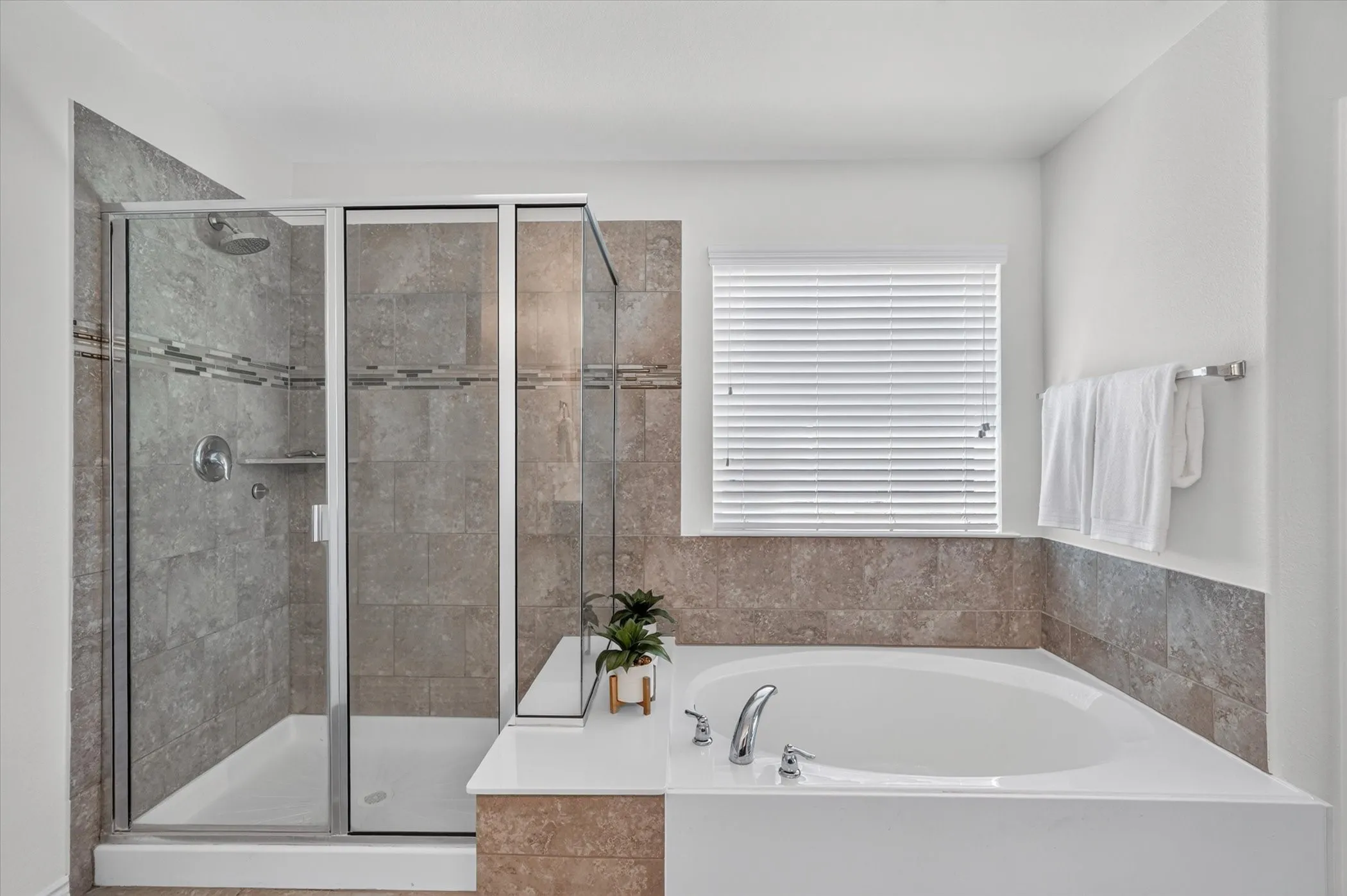 Walk-in shower with clear glass enclosure and built-in shelving, accompanied by a corner soaking tub with deck-mounted fixtures