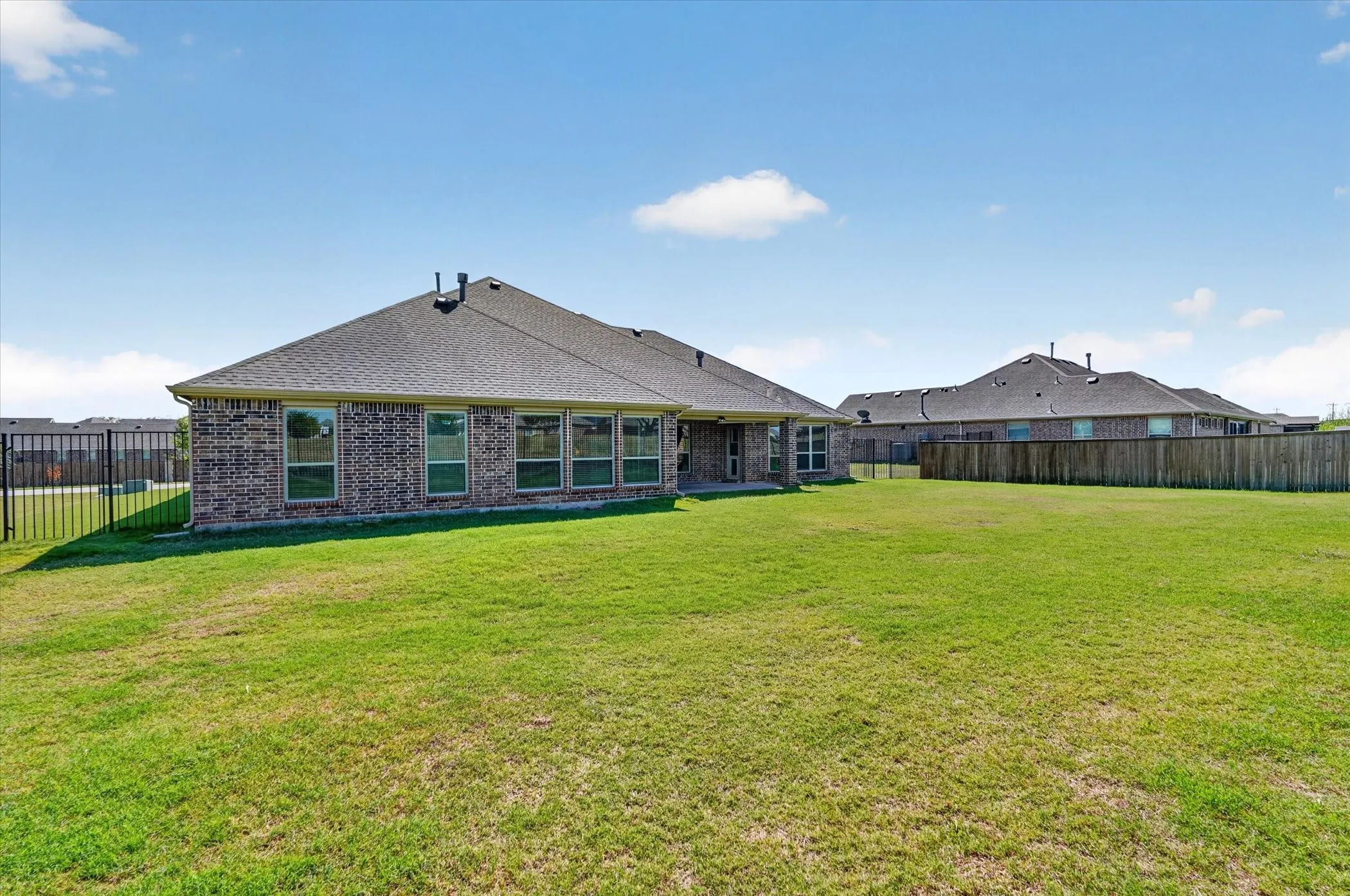 Expansive green lawn with a brick exterior, multiple windows, and a black metal fence