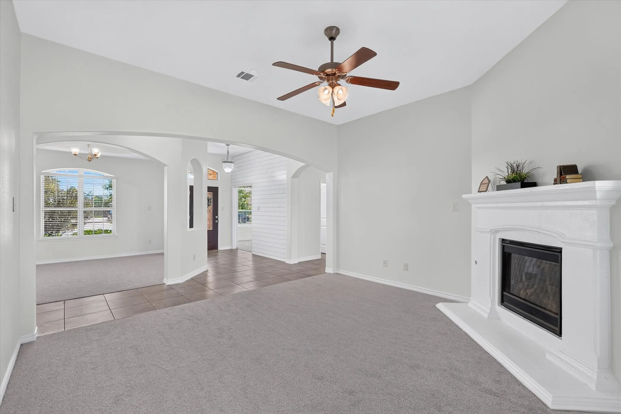 Central living space with vaulted ceilings, a ceiling fan, a fireplace with a white mantel, and arched doorways
