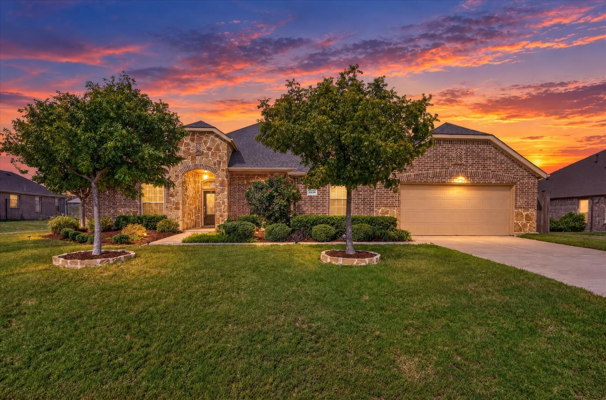 Brick and stone facade, arched entry, attached garage, concrete driveway, and manicured landscaping