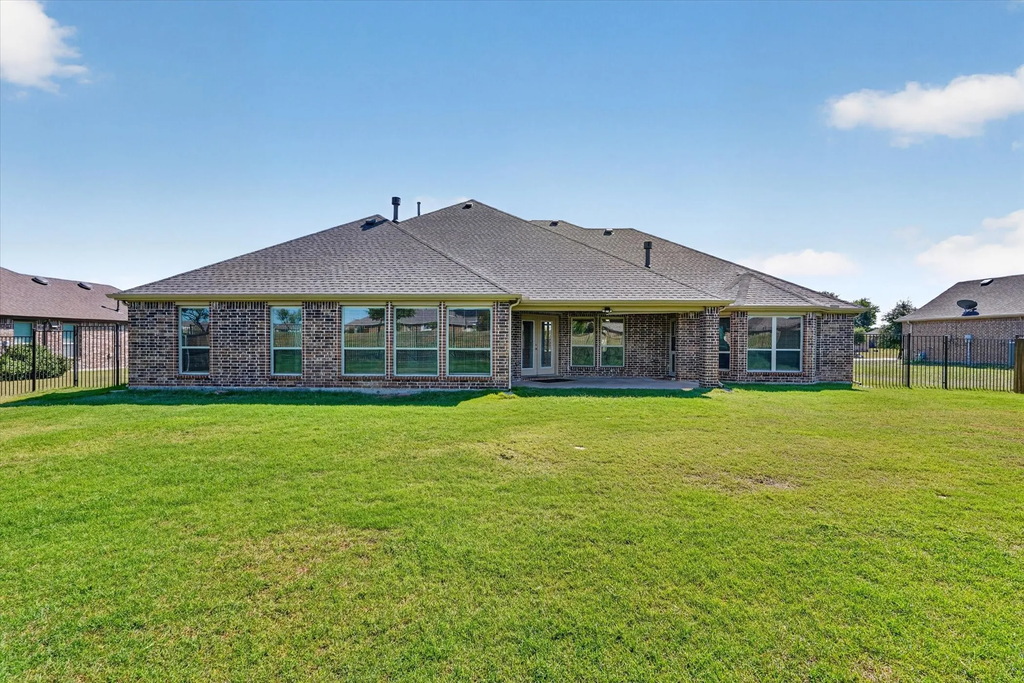Expansive backyard featuring a manicured lawn, brick exterior, and covered patio