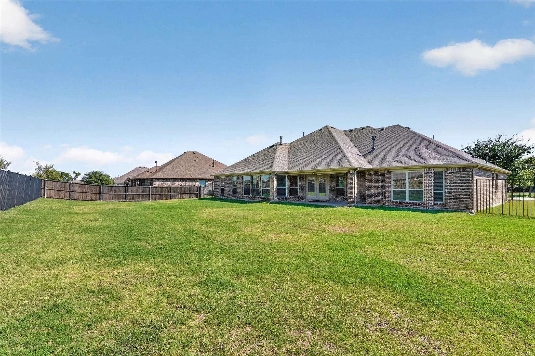 Expansive grass lawn with a full privacy fence and brick exterior