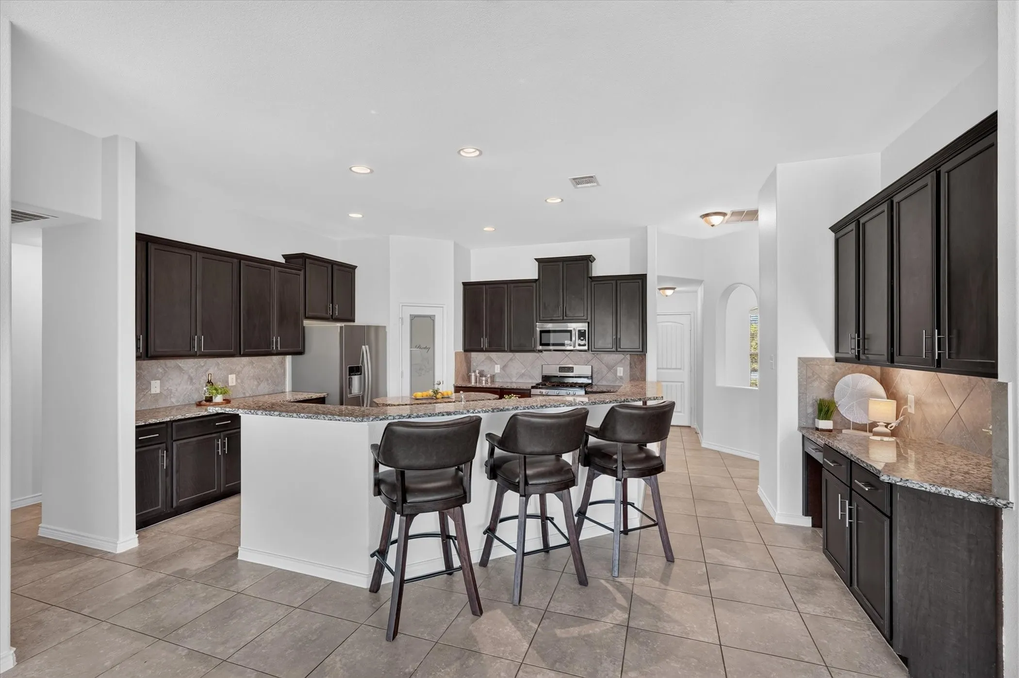 Expansive kitchen featuring dark wood cabinetry, granite countertops, tile backsplash, and recessed lighting
