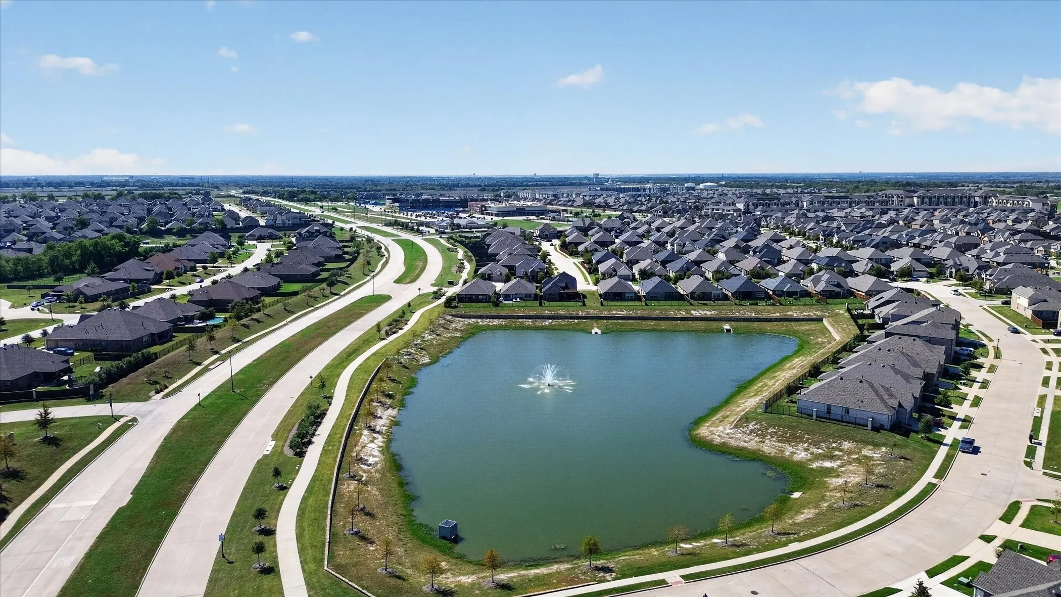 Residential neighborhood featuring numerous single-story homes, an expansive retention pond with a fountain, and paved roadways with sidewalks