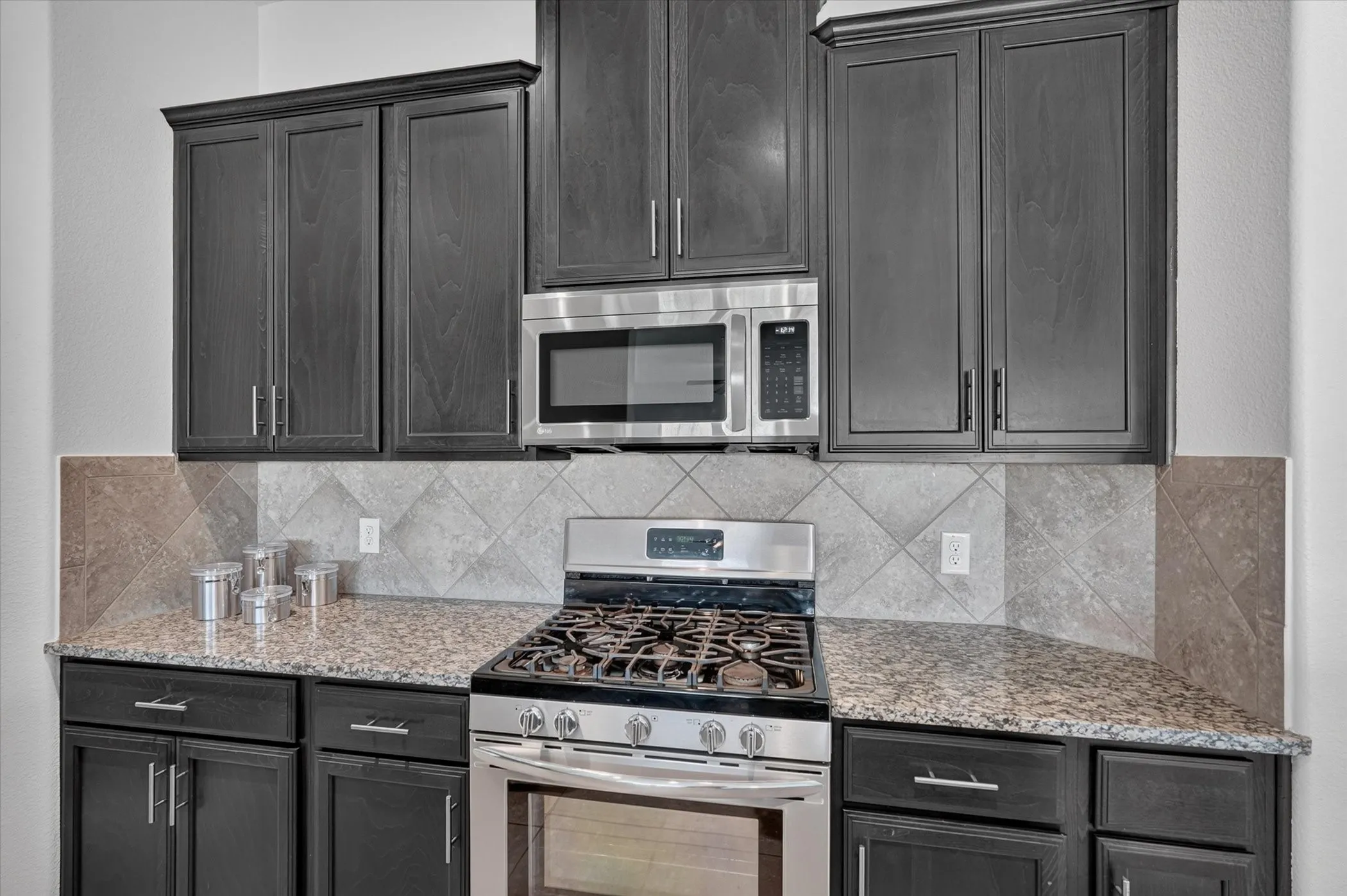 Stainless steel range with oven, built-in microwave, granite countertops, dark-toned cabinetry, and a patterned tile backsplash