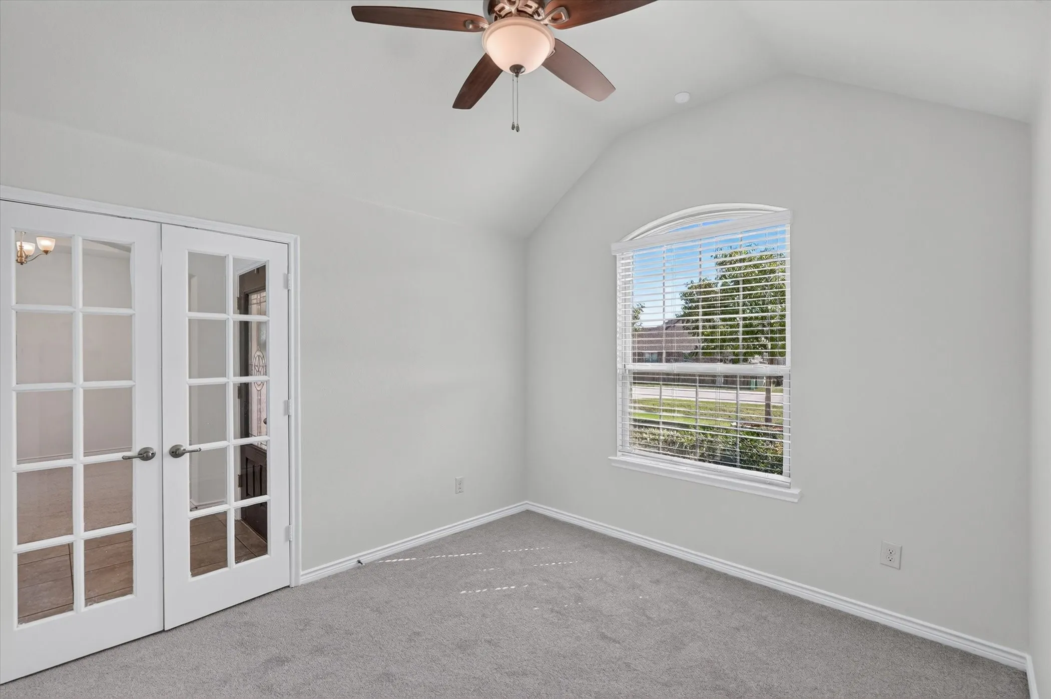 Vaulted ceiling featuring a ceiling fan with integrated lighting, arched window, French doors, and neutral carpeting