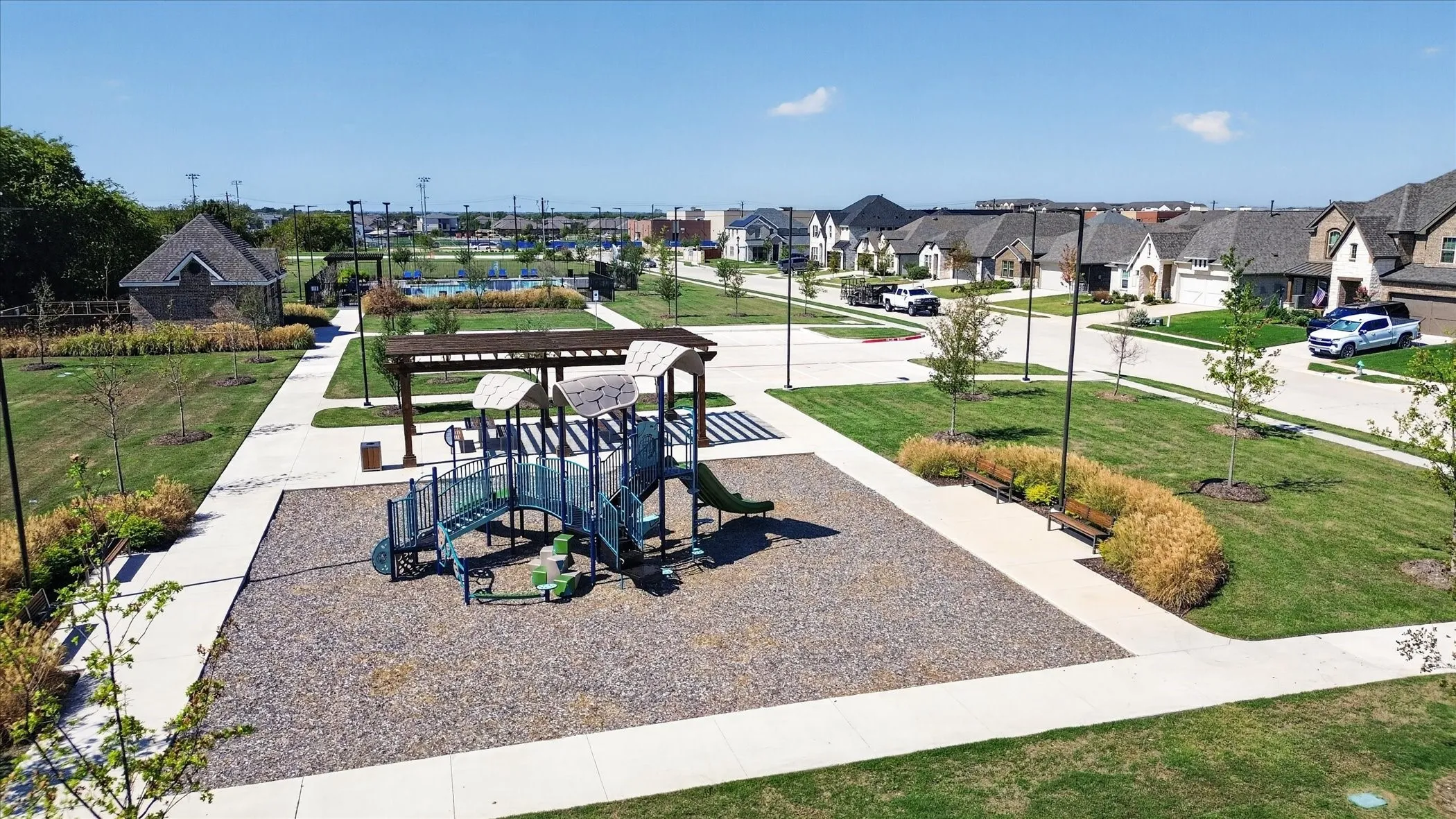 Community playground with a shaded structure, surrounding green spaces, and paved pathways