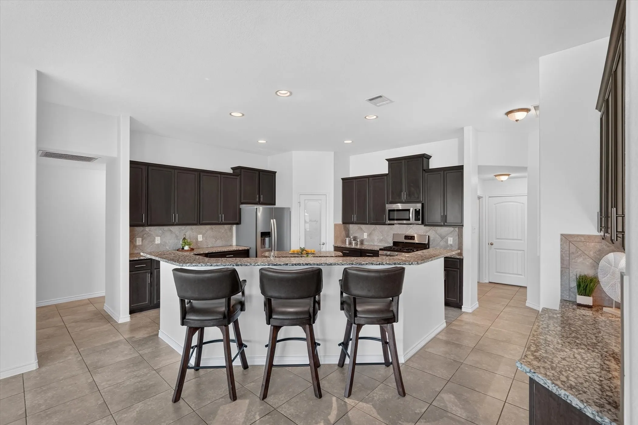 Kitchen featuring dark wood-finish cabinetry, granite countertops, stainless steel appliances, a tiled backsplash, and recessed lighting