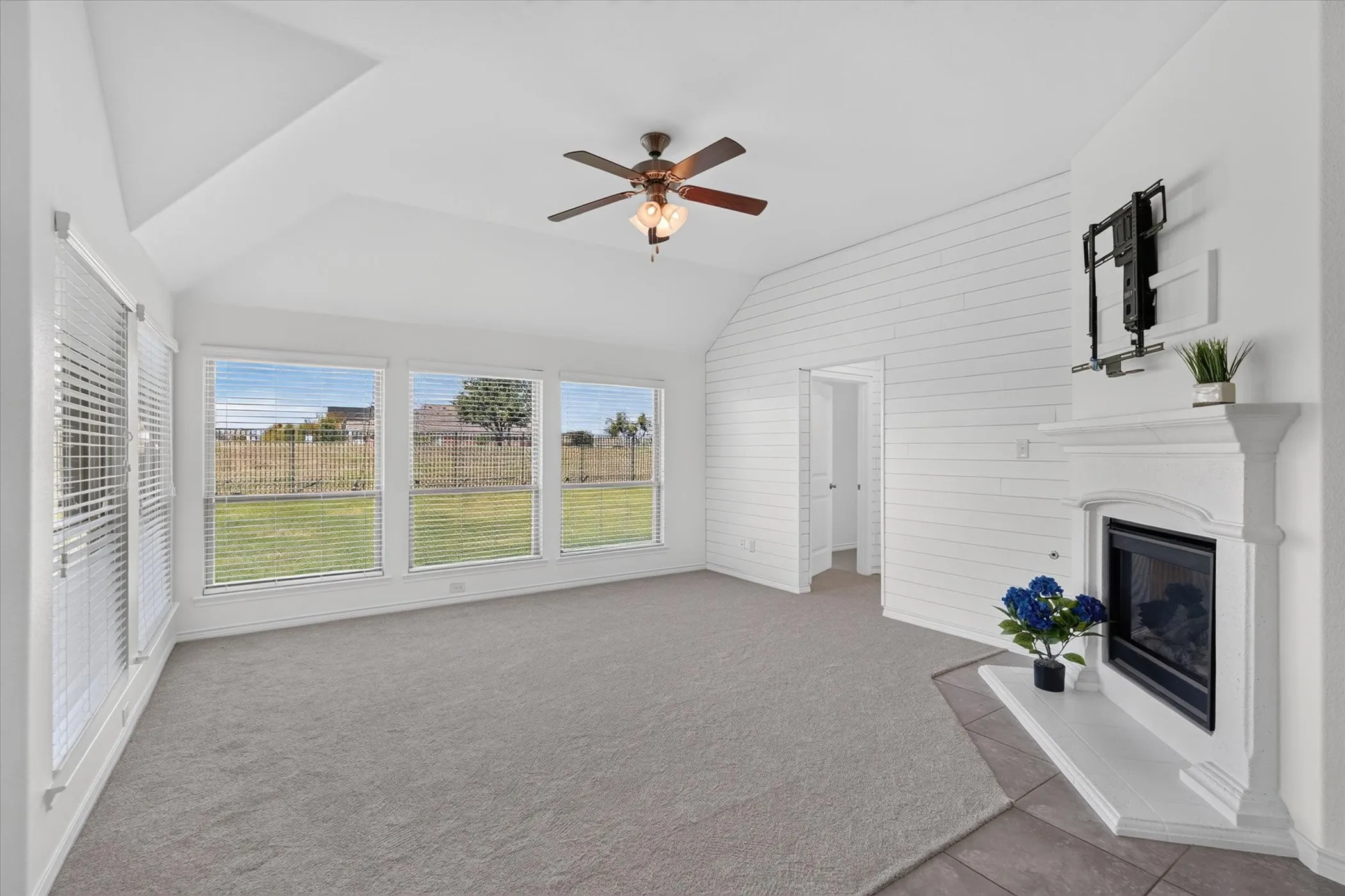 Vaulted ceiling, ceiling fan, fireplace with mantel, window blinds, and shiplap accent wall