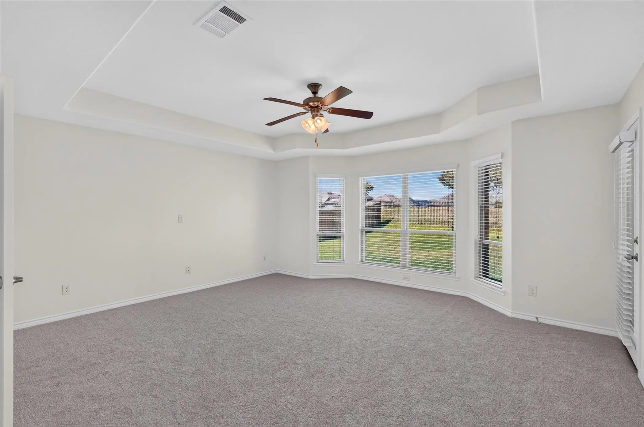 Tray ceiling with a ceiling fan, bay window configuration, and gray carpeting