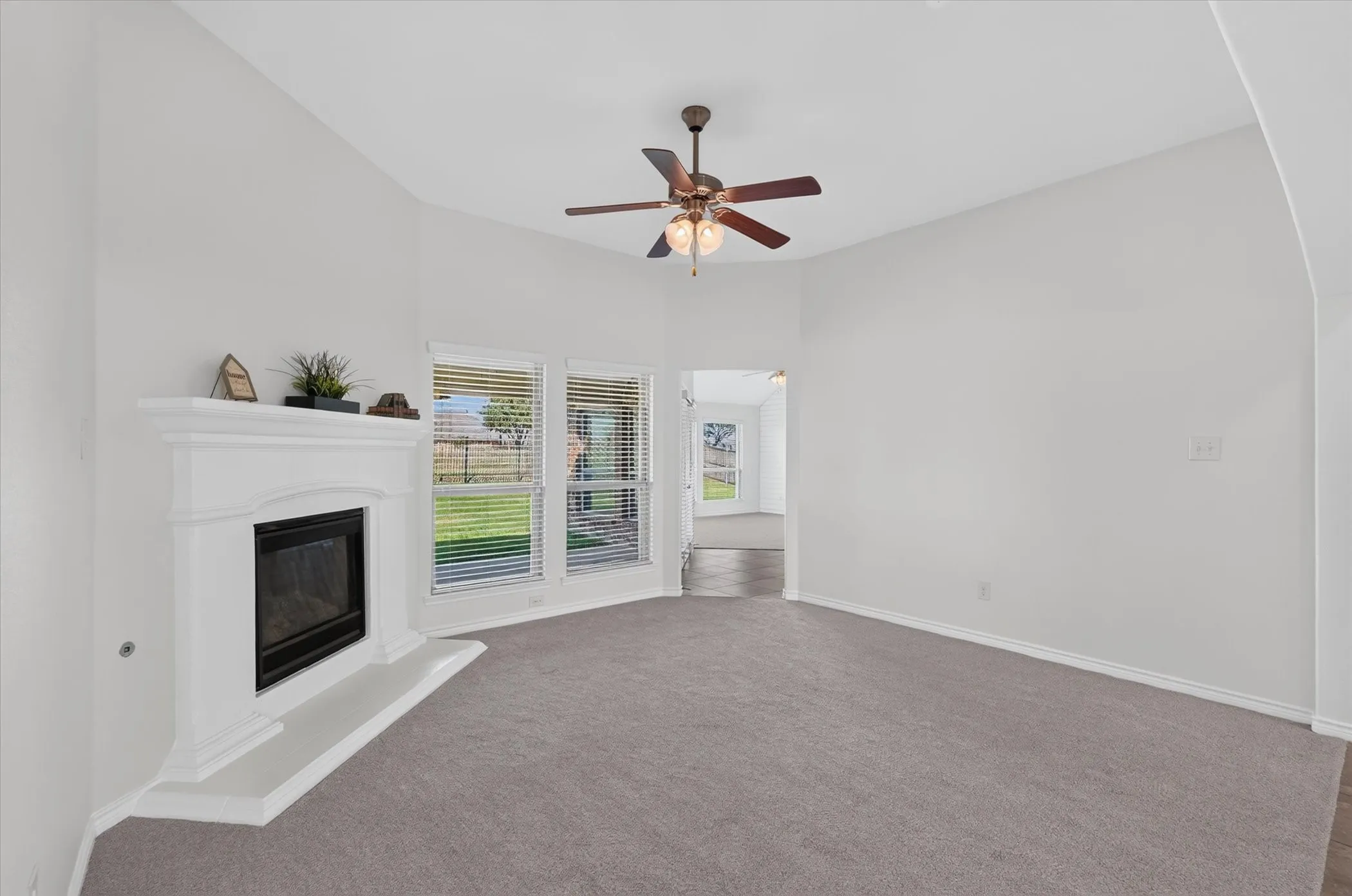 Vaulted ceiling, corner fireplace, recessed hearth, multiple windows, and a ceiling fan with integrated lighting