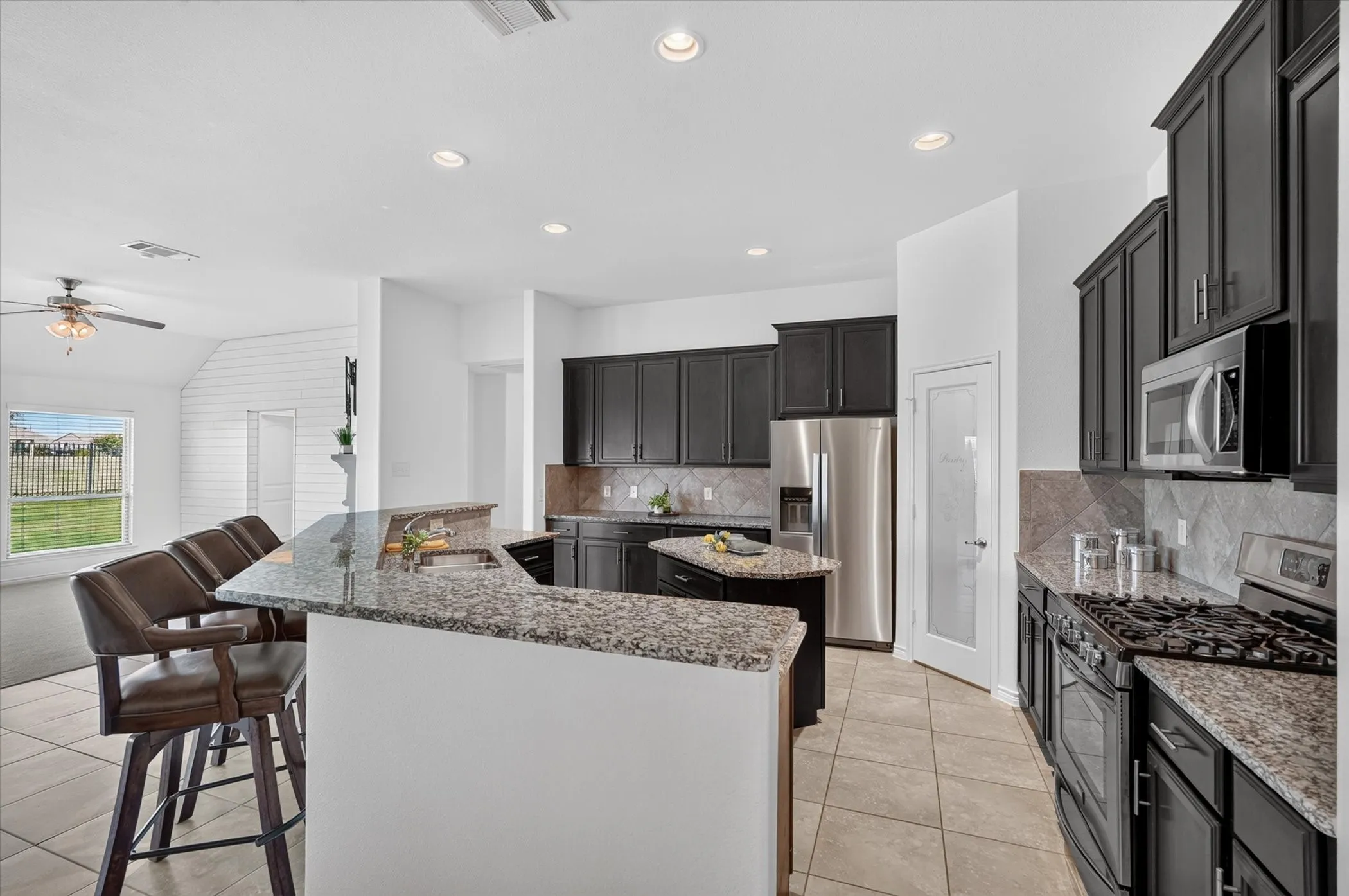 Kitchen featuring dark cabinetry, granite countertops, stainless steel appliances, and a tiled backsplash