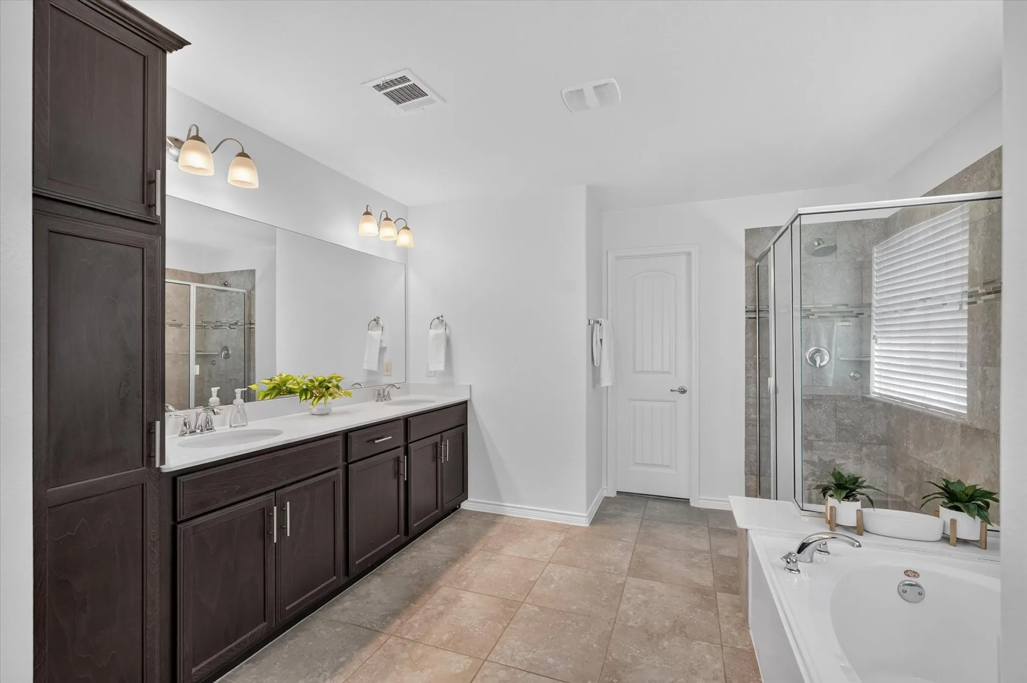 Dual vanity with white undermount sinks, dark wood-finish cabinetry, built-in storage cabinet, enclosed glass shower, and a built-in soaking tub