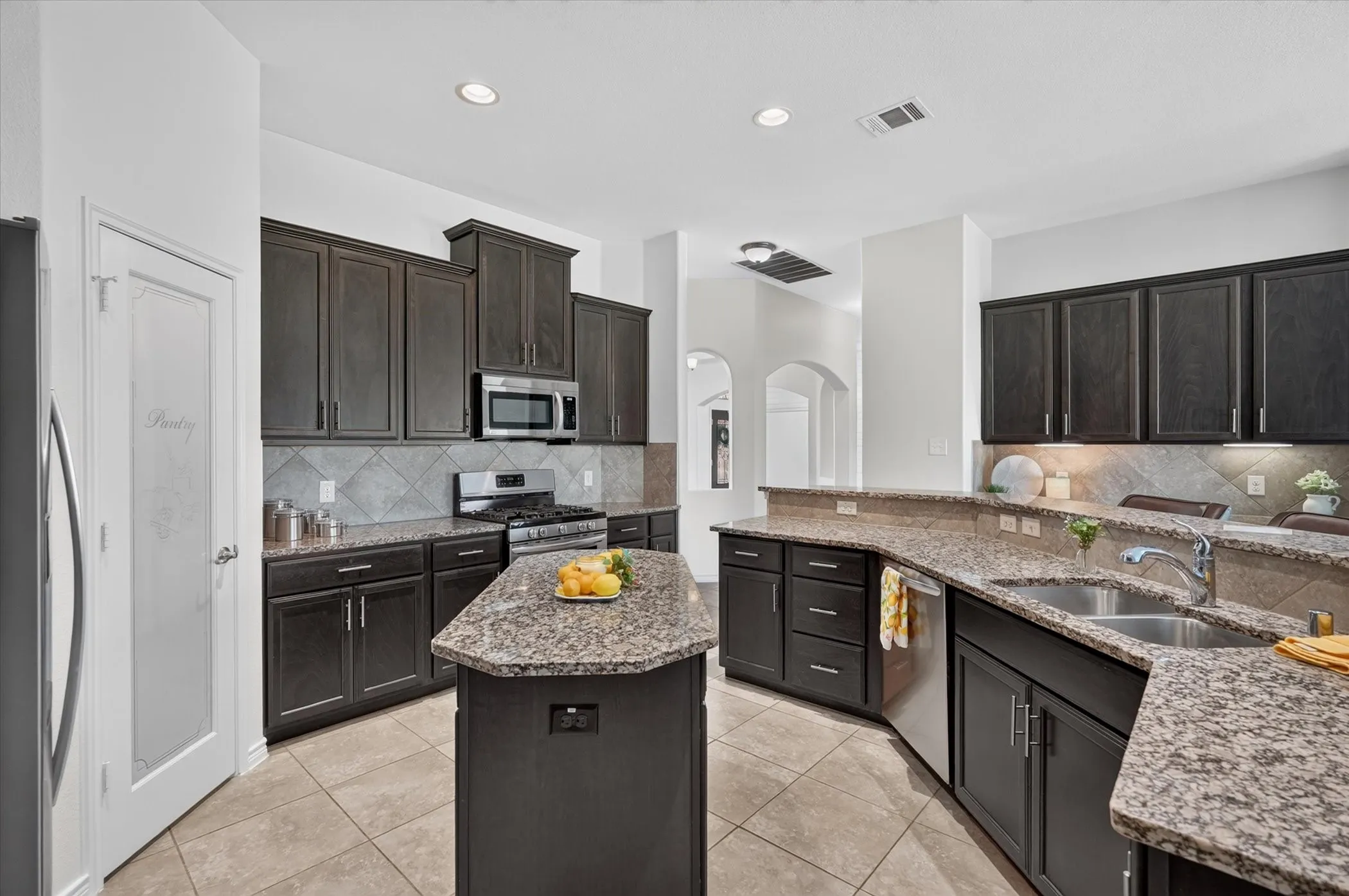 Kitchen featuring dark wood-finish cabinetry, granite countertops, stainless steel appliances, a tiled backsplash, and recessed lighting