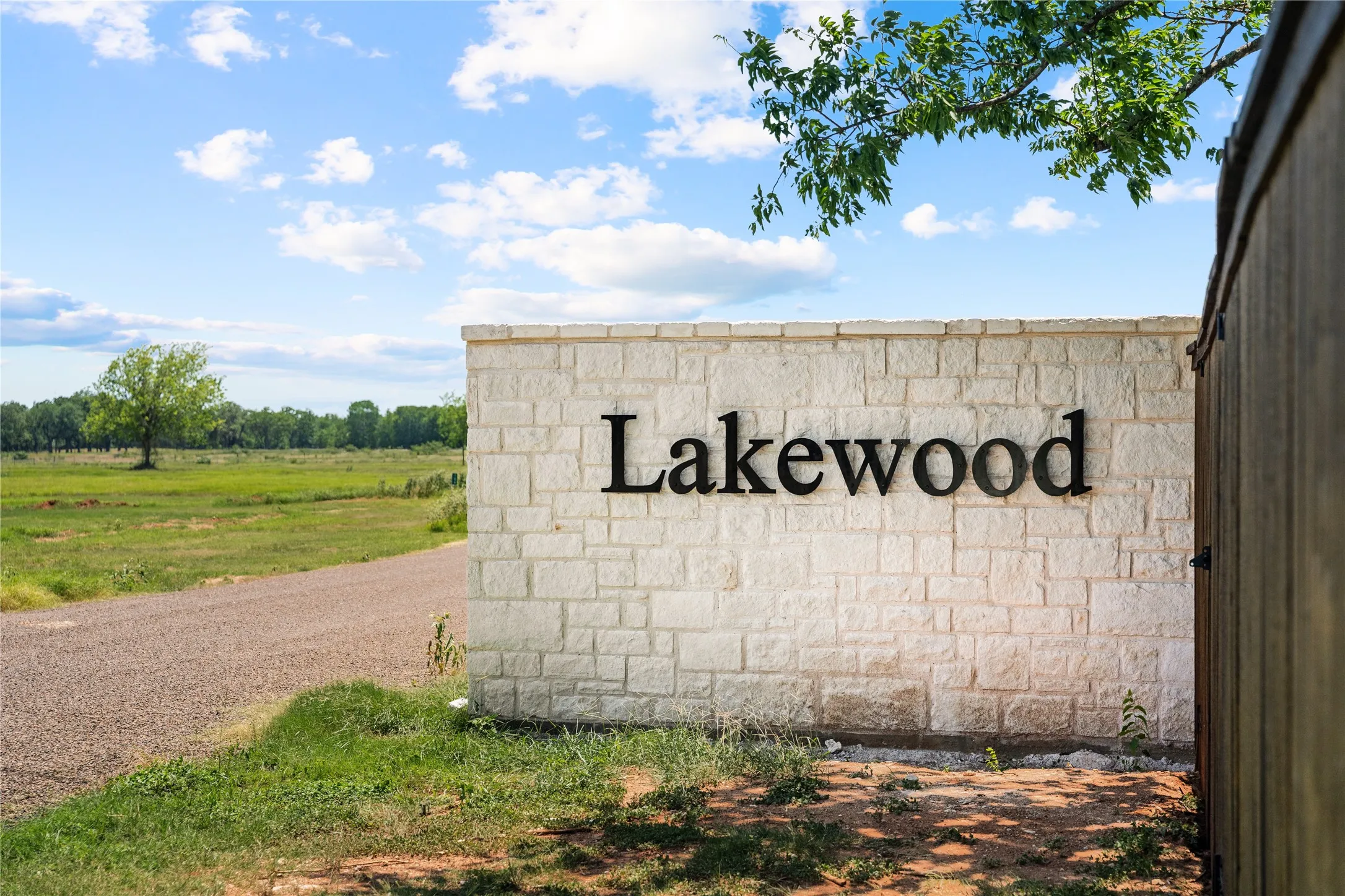 Stone-clad entrance wall featuring dimensional lettering and a gravel road leading to open grounds