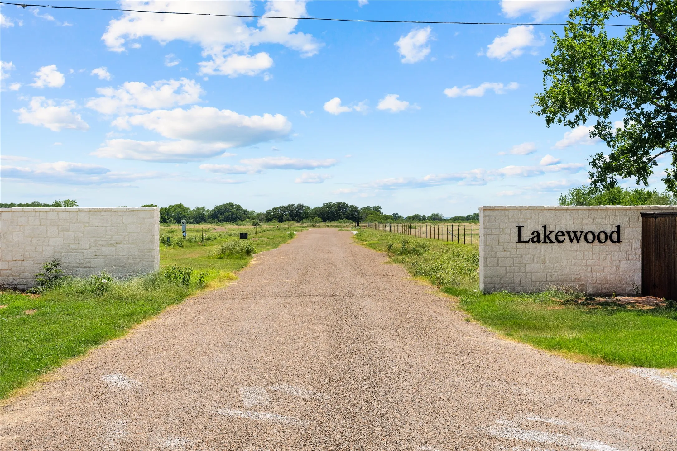 Gravel access road with stone block entrance walls and a "Lakewood" sign
