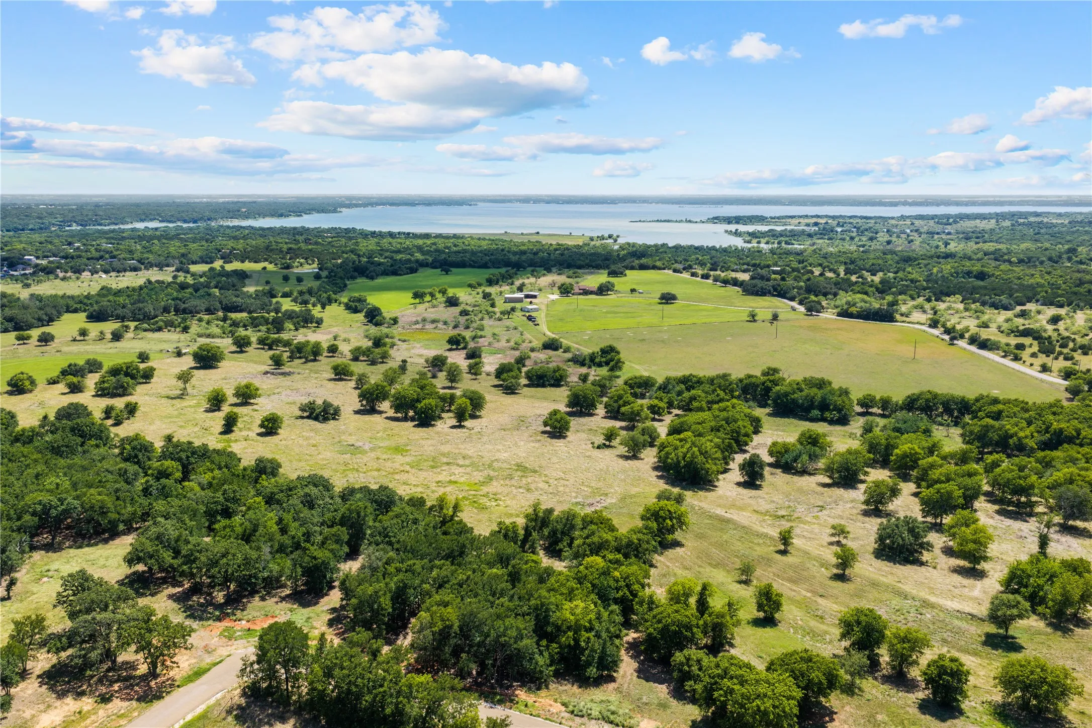 Expansive rural landscape featuring a large body of water, scattered trees, and open fields