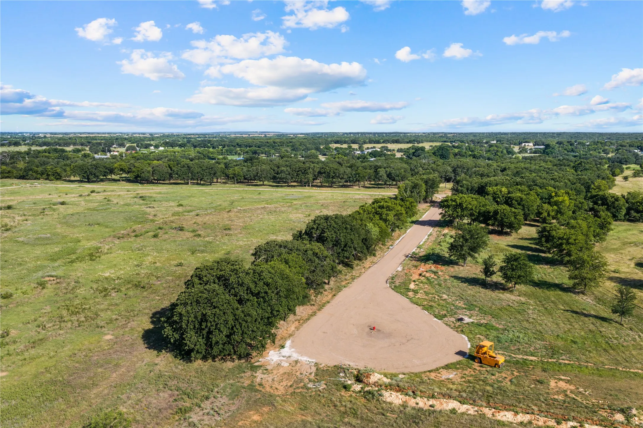 Expansive undeveloped land with a partial gravel road and numerous mature trees