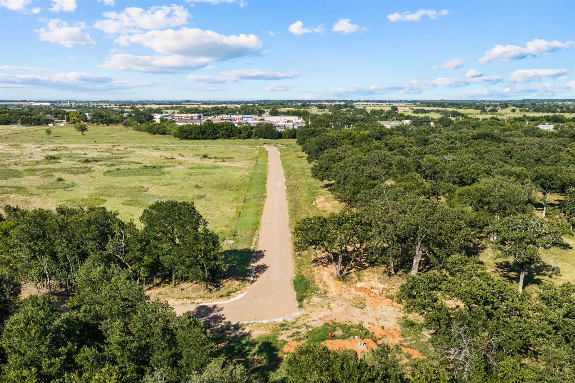 Expansive land parcel featuring a central unpaved road, bordered by mature trees and open grassy areas