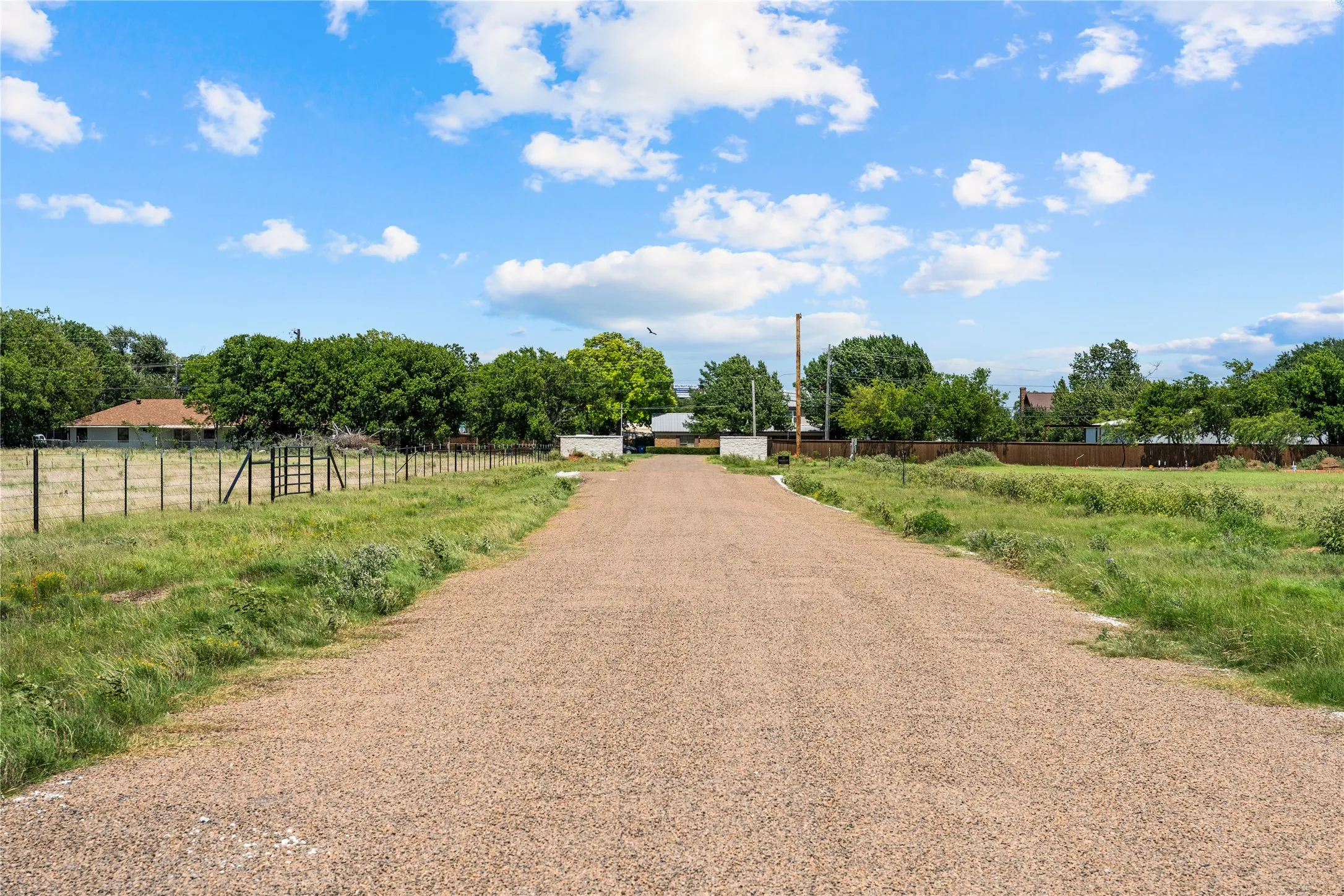 Gravel driveway extending through a grassy expanse with mature trees