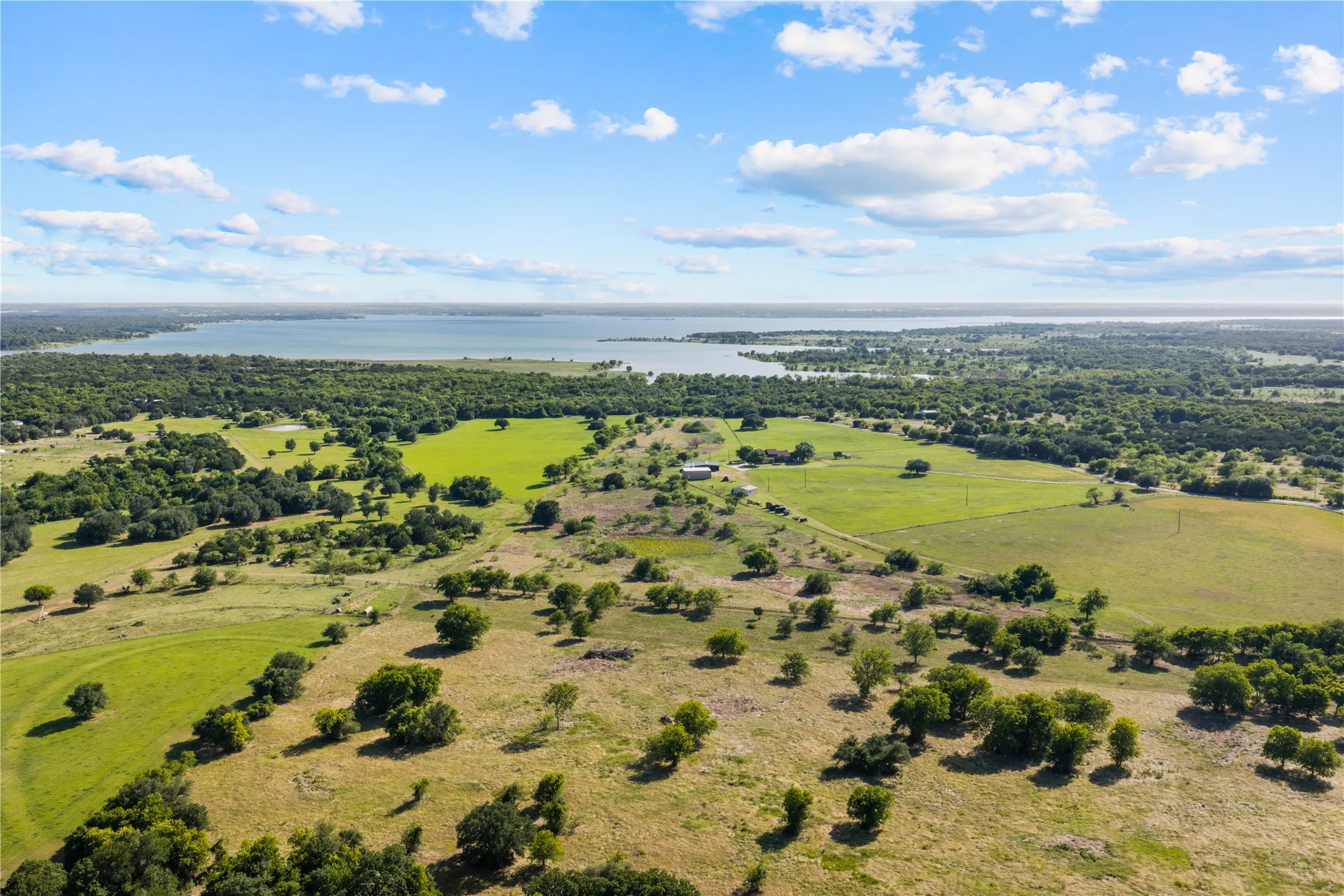 Expansive land parcel featuring open fields, scattered mature trees, and distant water frontage