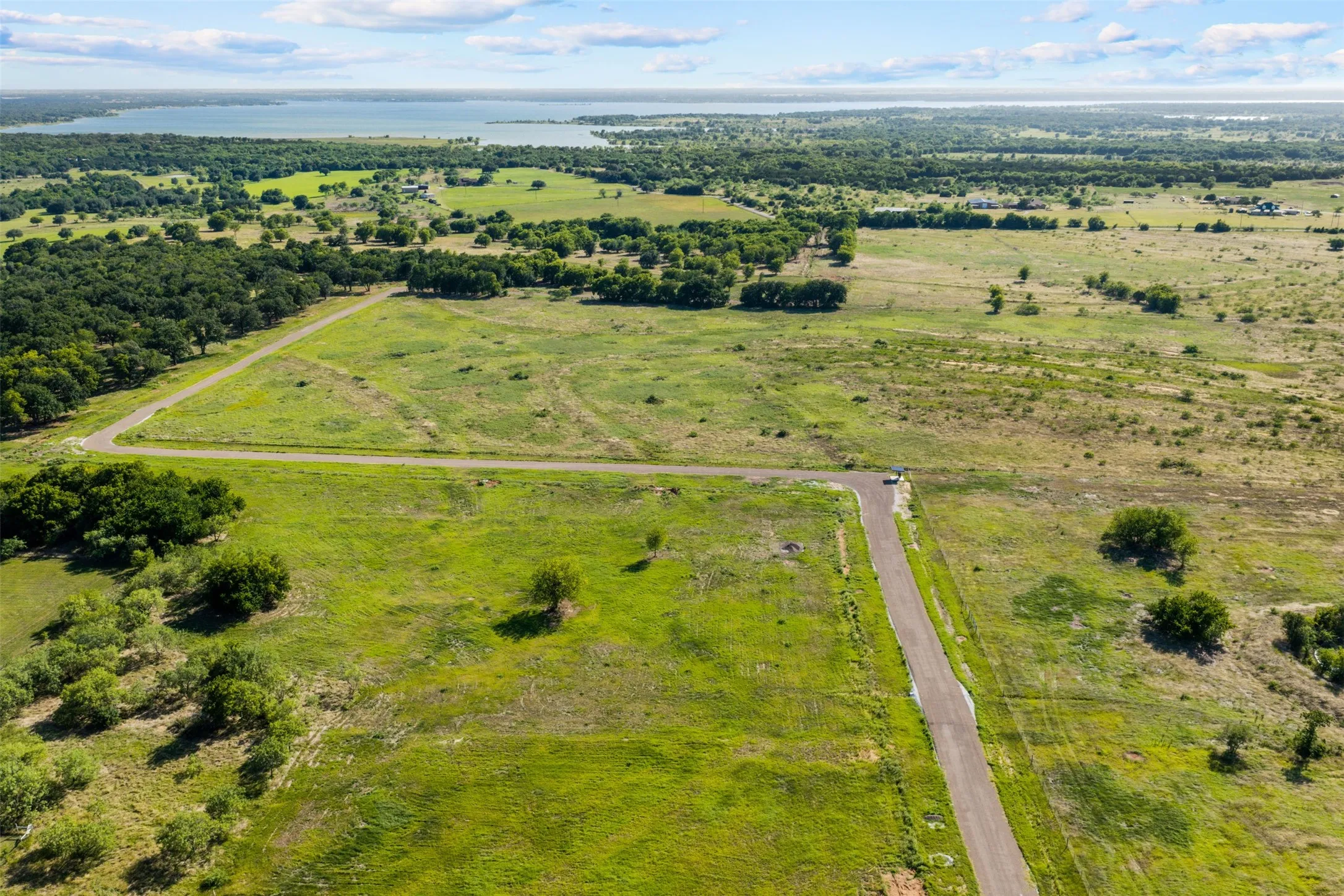 Expansive acreage featuring a paved roadway, scattered trees, and a distant lake