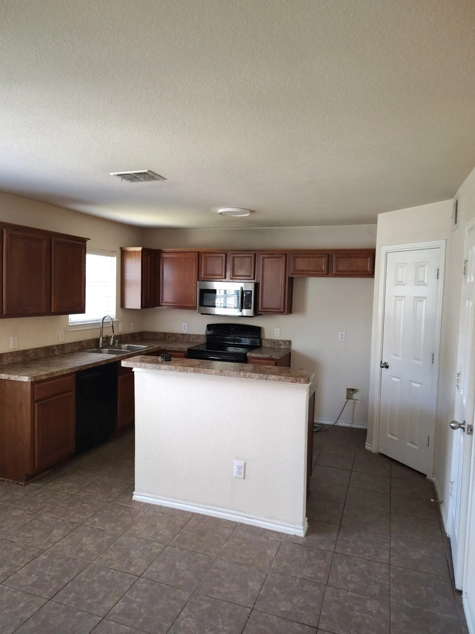 Kitchen featuring warm-toned cabinetry, a stainless steel microwave, black electric range, and a breakfast bar