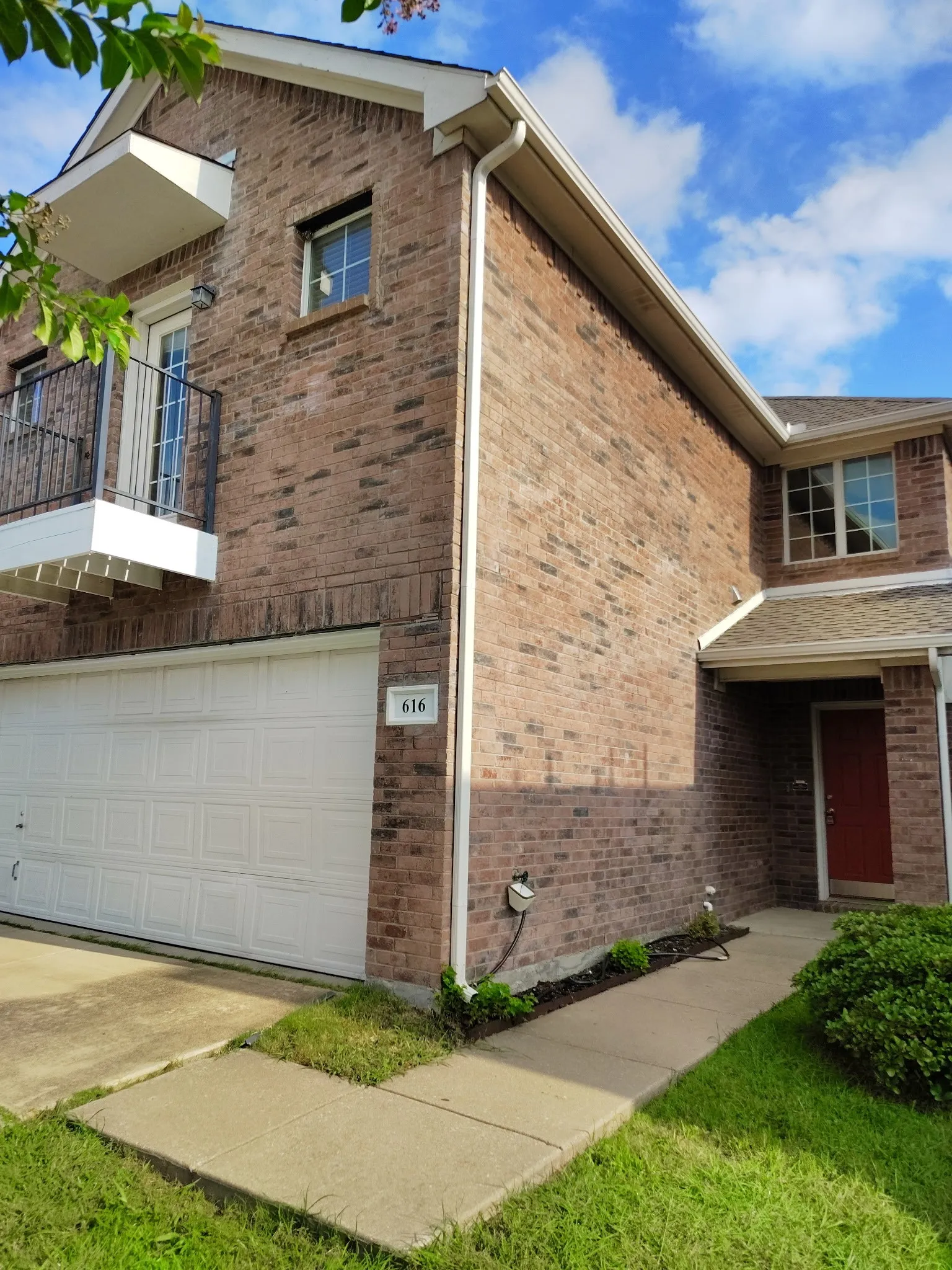 Brick exterior with an integrated garage, red entry door, and a second-story balcony