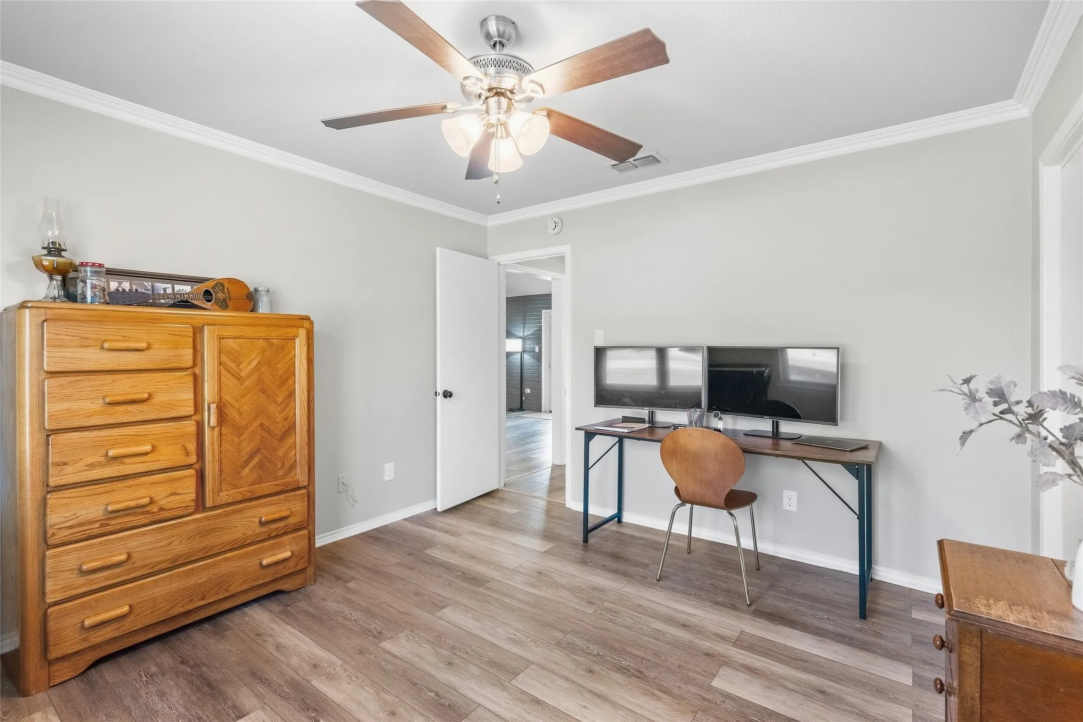 Wood-finish flooring, light gray wall paint, white trim, ceiling fan with light kit, and a white interior door