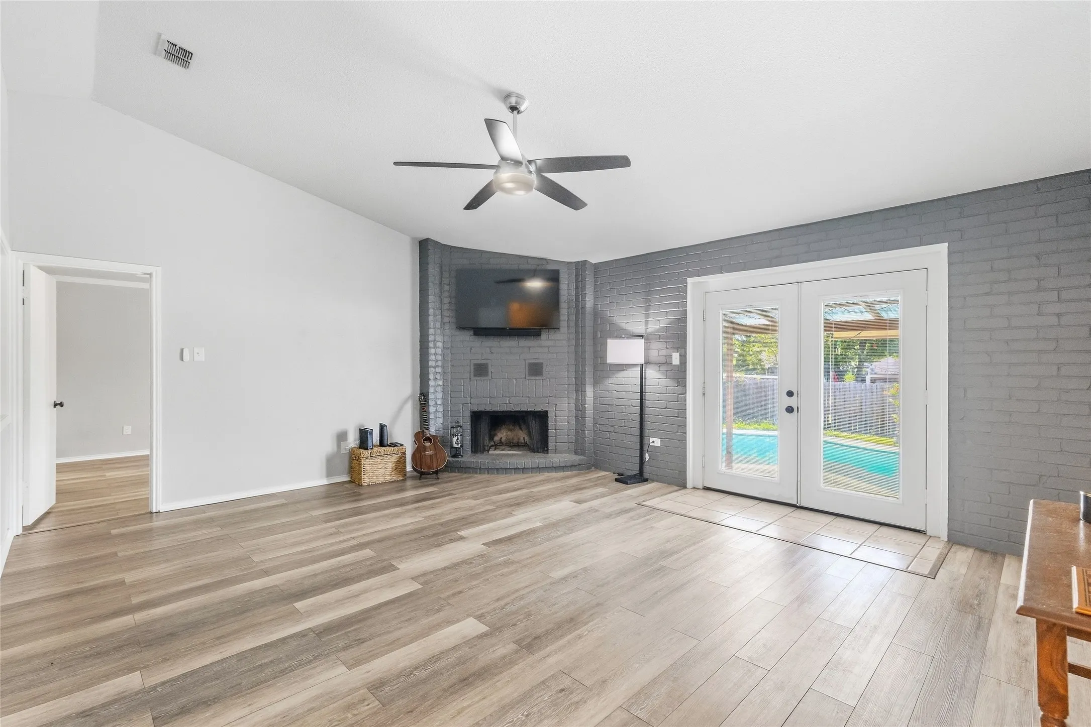 Vaulted ceiling with a ceiling fan, corner brick fireplace, wood-finish flooring, and French doors opening to a pool
