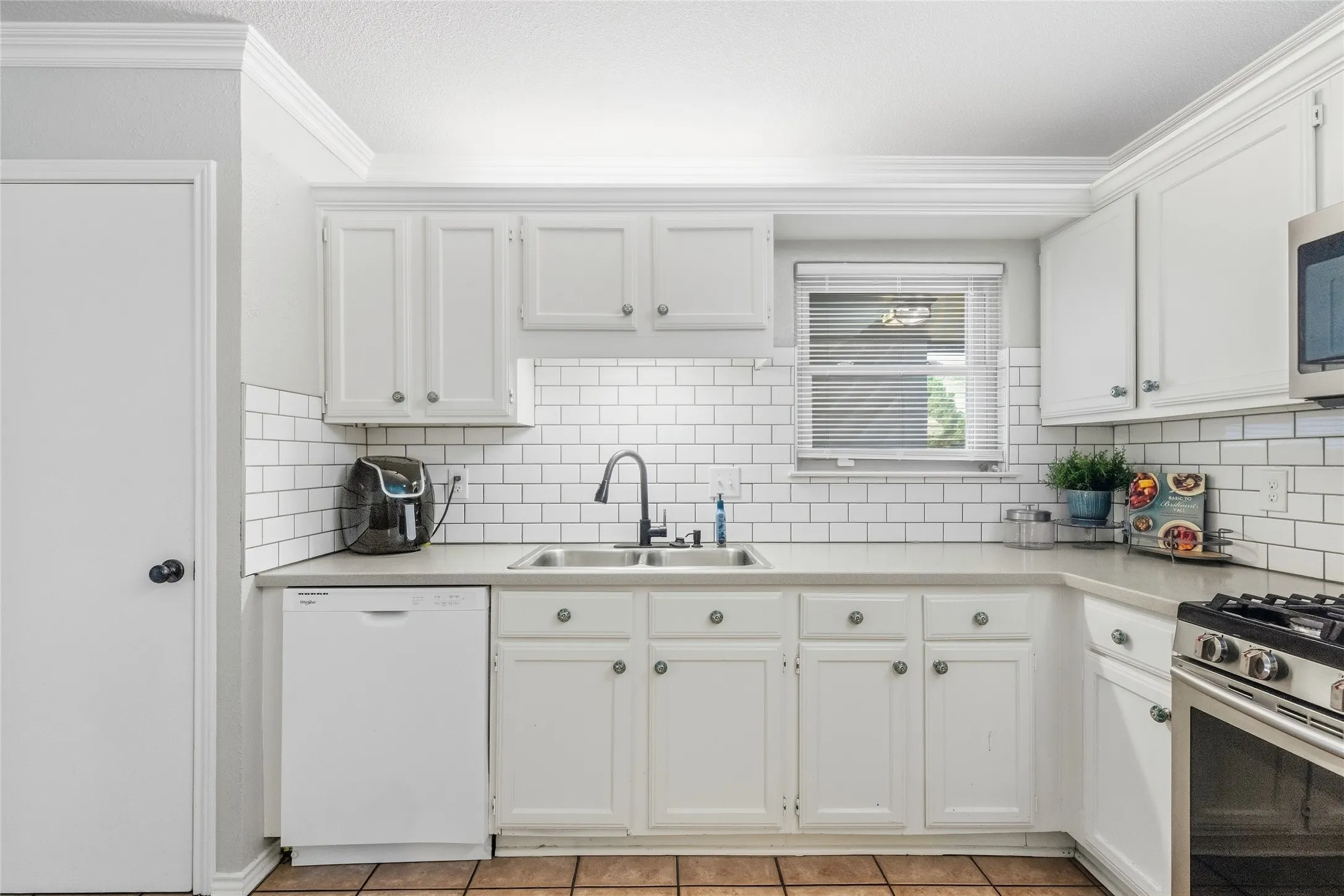 White cabinetry, subway tile backsplash, stainless steel sink, pull-down faucet, and durable countertops