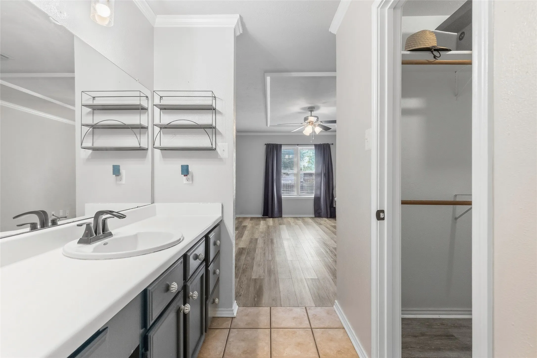 Vanity with an integrated sink and brushed nickel faucet, large mirror, built-in shelving, and tile flooring