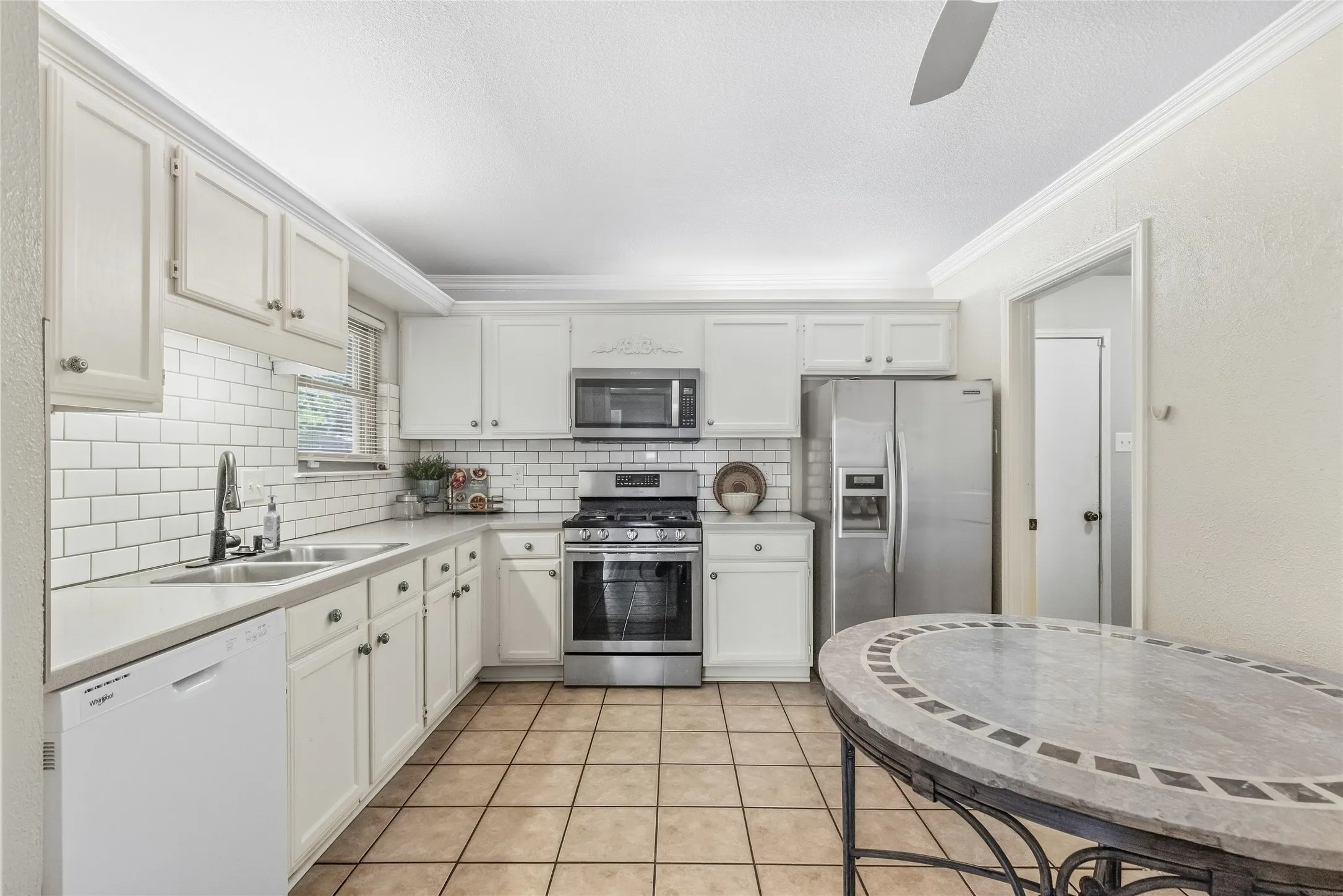 White cabinetry with crown molding, subway tile backsplash, stainless steel appliances, and tile flooring