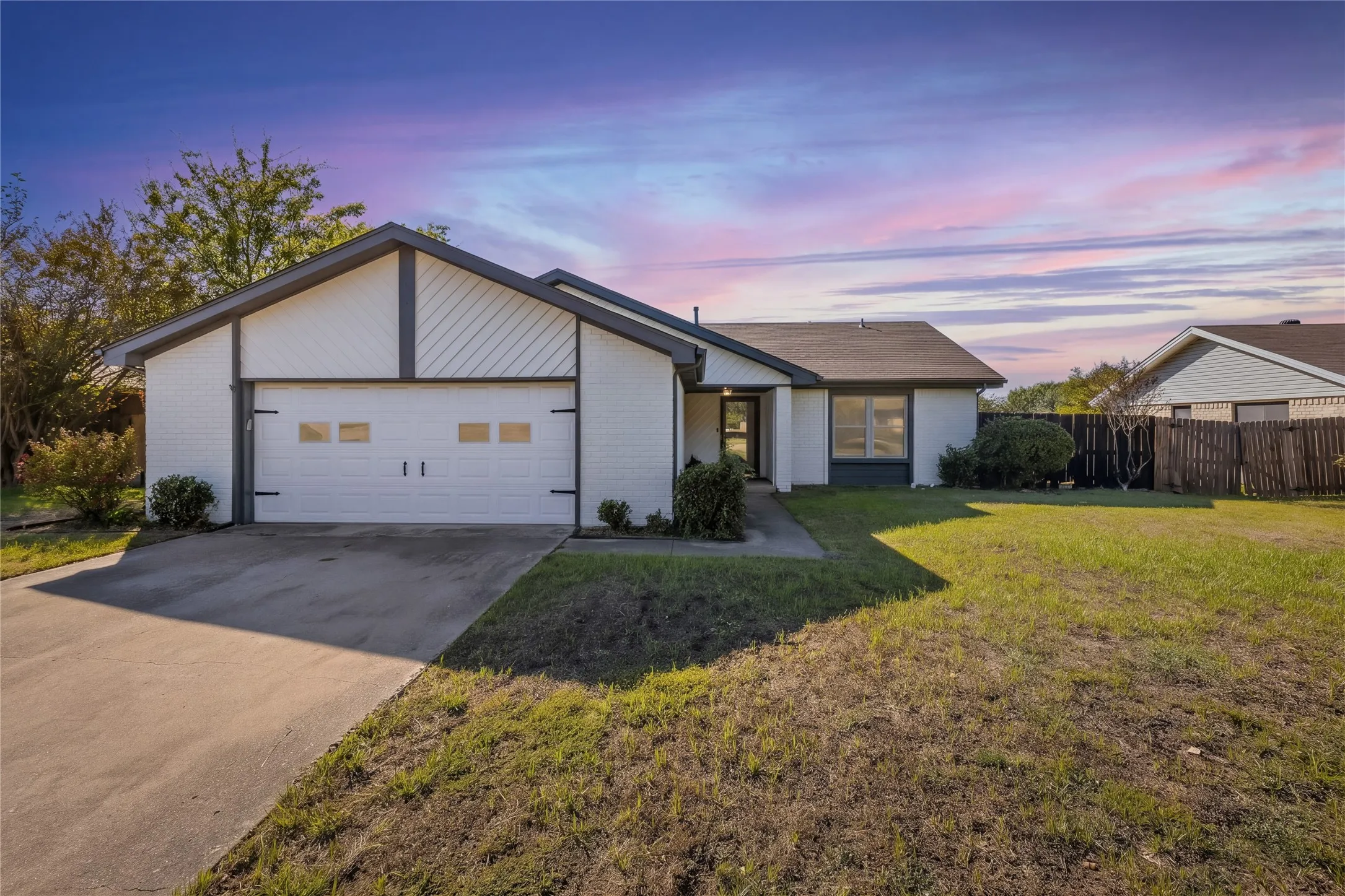 White brick exterior, dark trim accents, attached garage with decorative hardware, concrete driveway, and front entry walkway