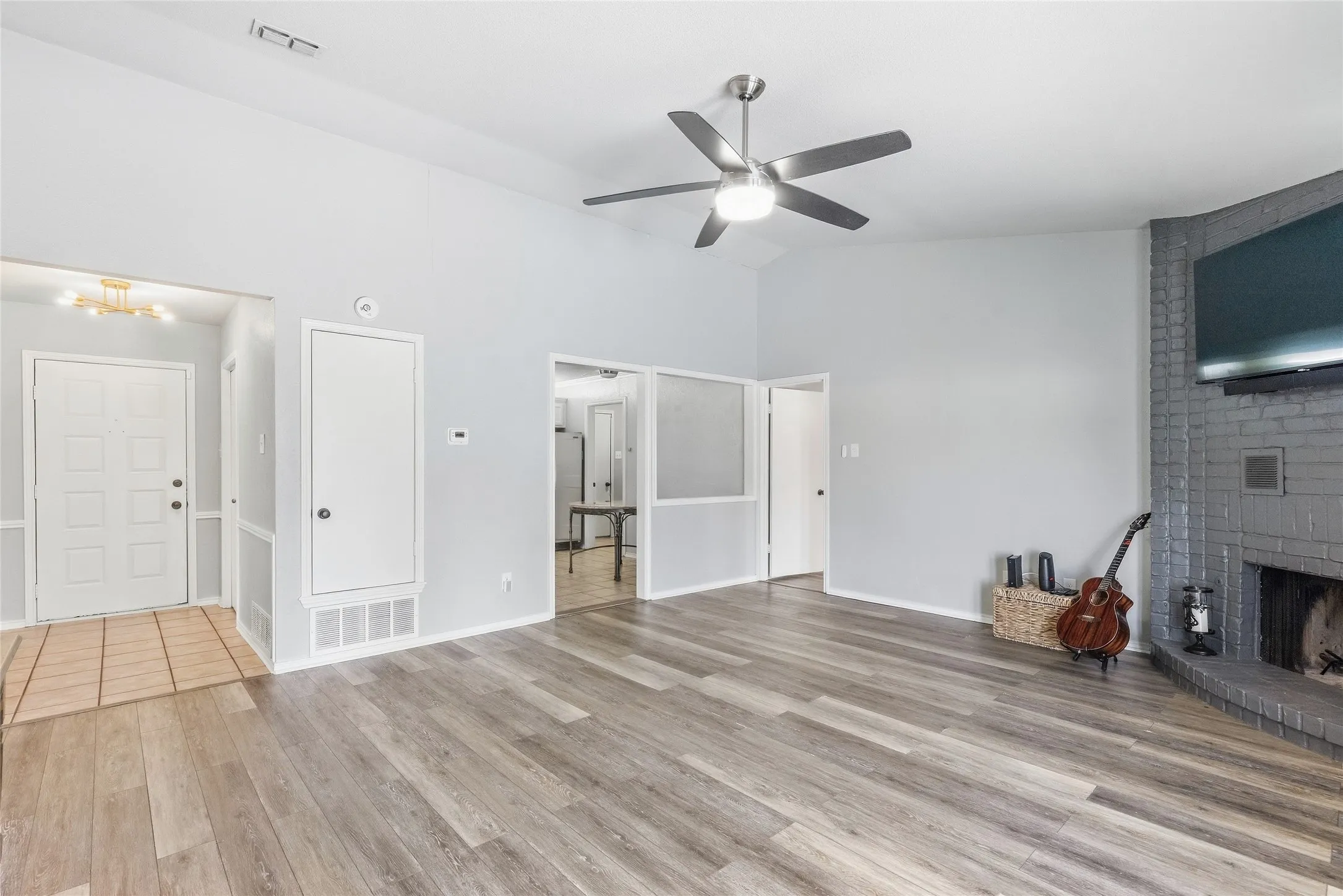 Vaulted ceiling with a ceiling fan, wood-finish flooring, brick fireplace, and a tiled entryway