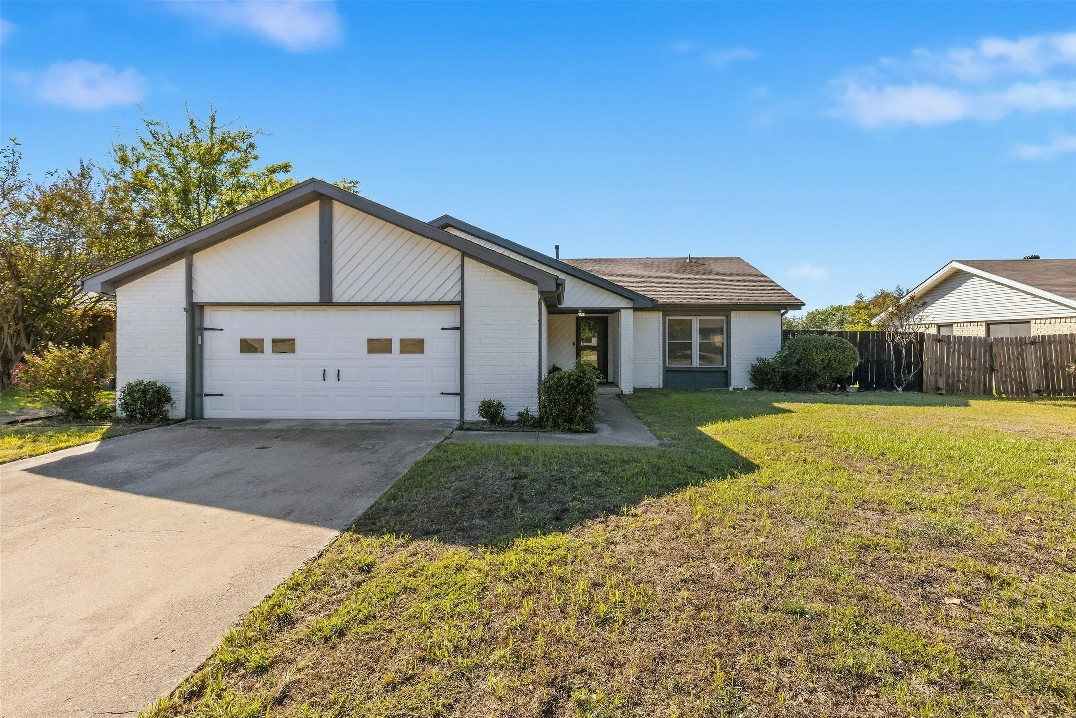 White brick exterior with a gray roof and trim, an attached garage with decorative hardware, a concrete driveway, and a front lawn