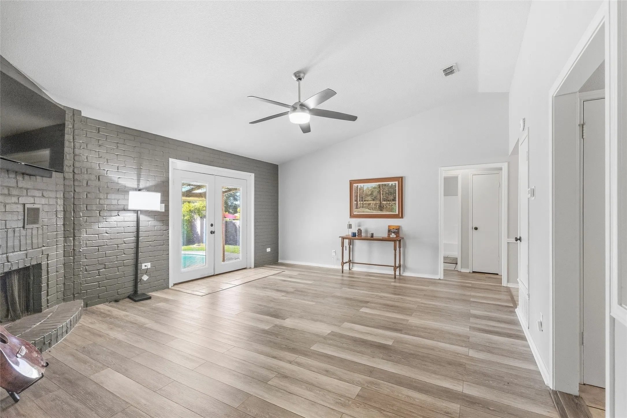 Vaulted ceiling, ceiling fan, wood-finish flooring, painted brick fireplace, double French doors