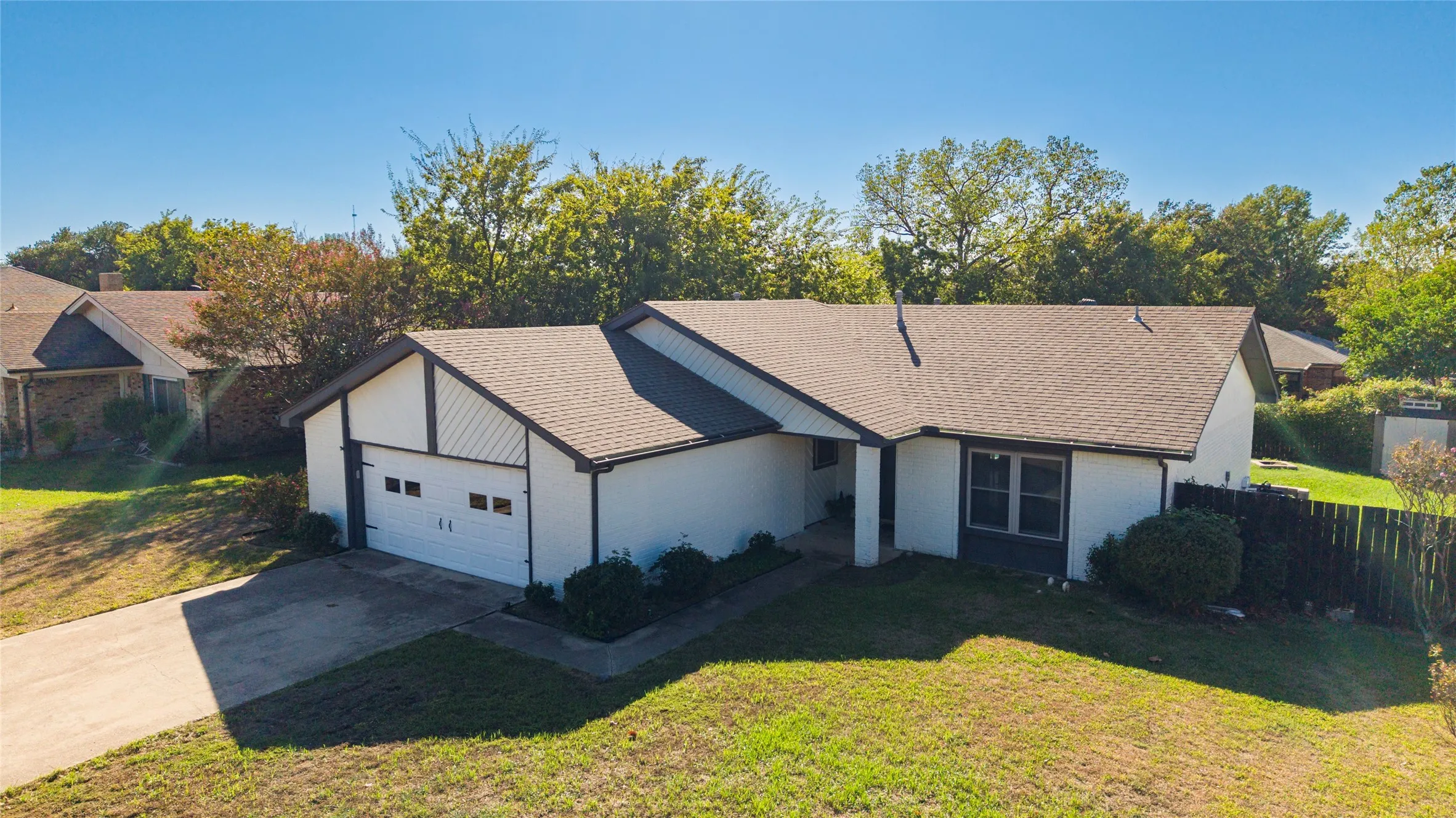 Single-story residence featuring a two-car garage, pitched shingle roof, and a privacy fence