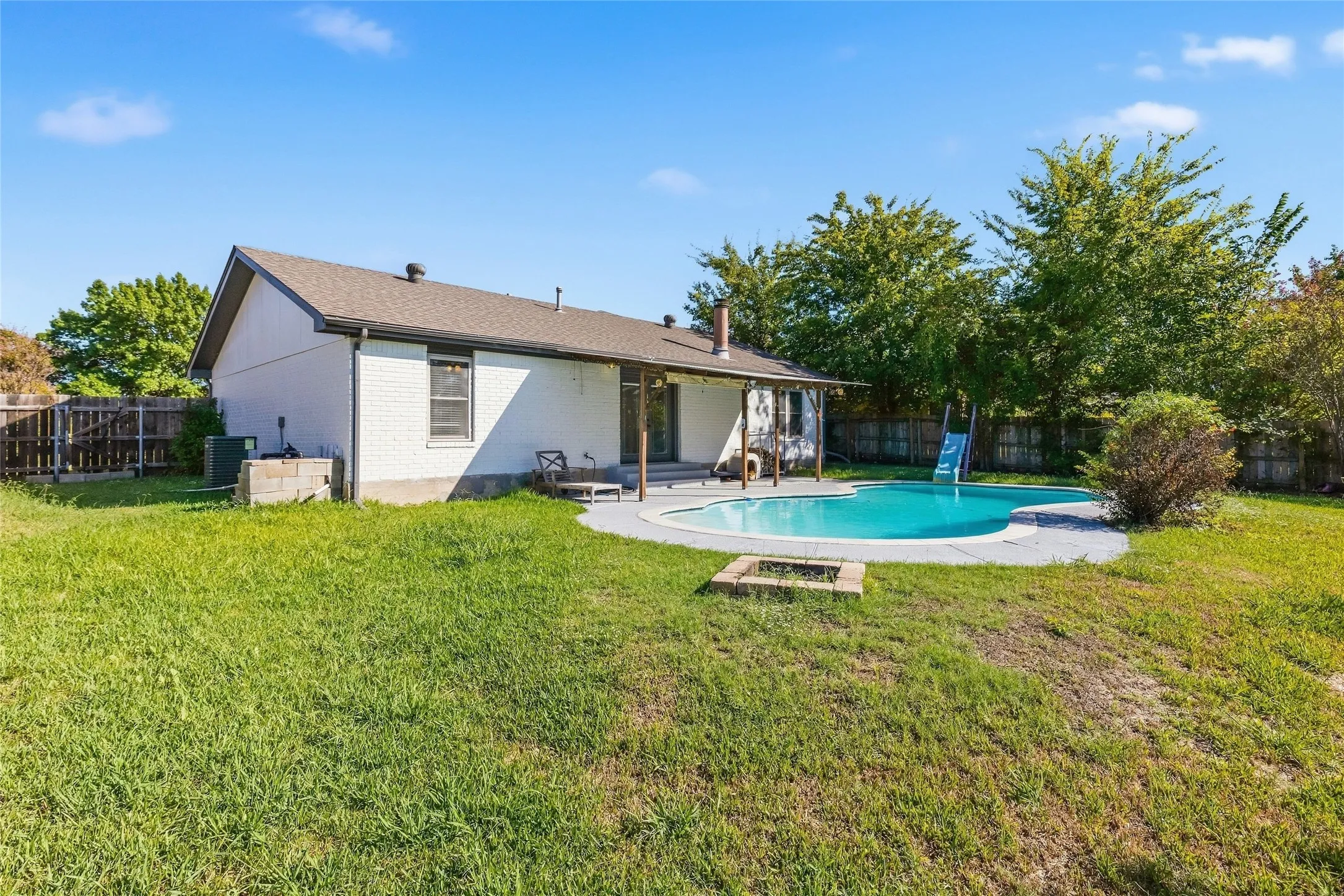 Spacious backyard featuring a built-in swimming pool, a covered patio, a fire pit, and a privacy fence