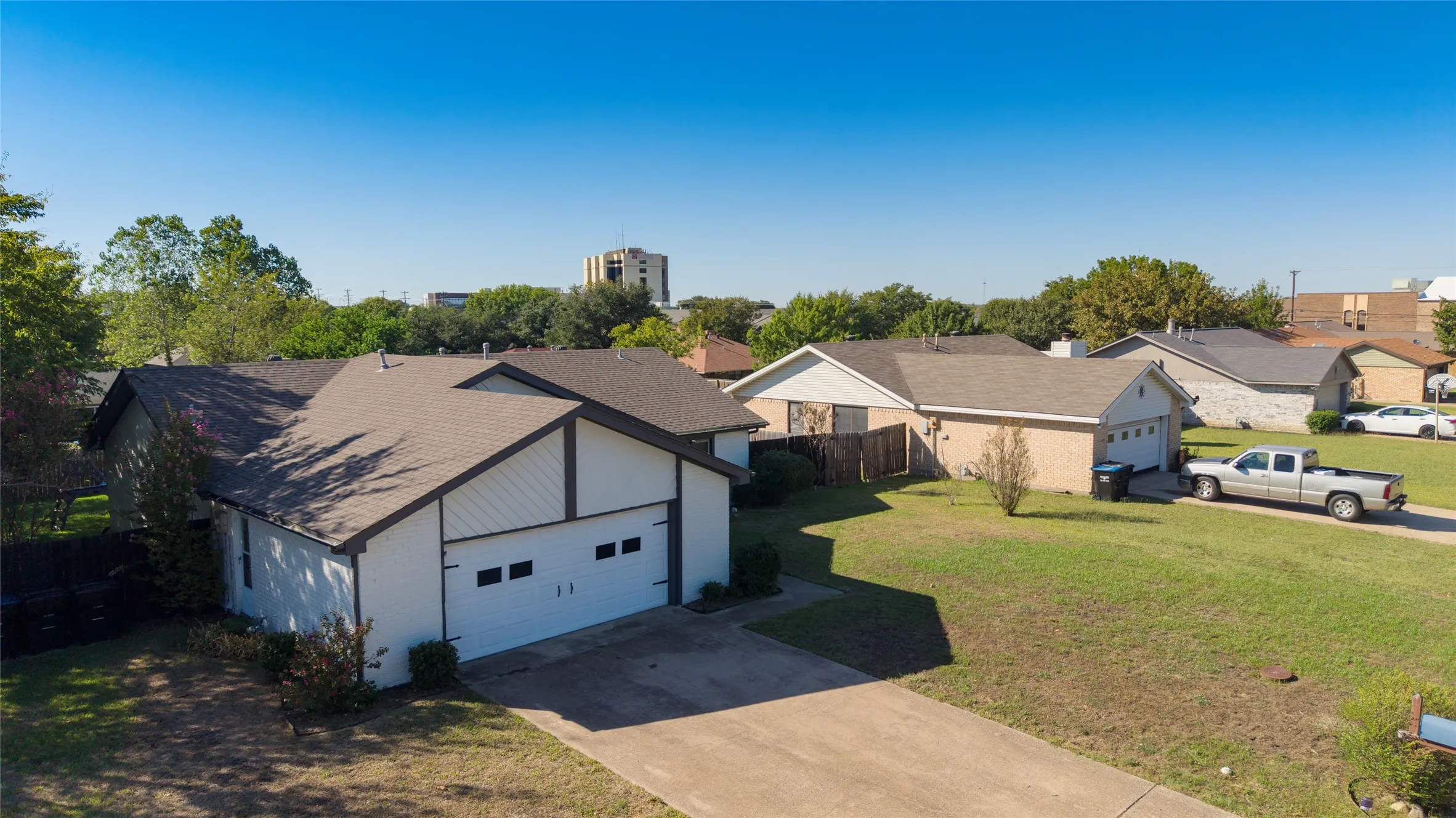 Expansive concrete driveway, white exterior siding, brown trim accents, attached two-car garage, and a lush green lawn