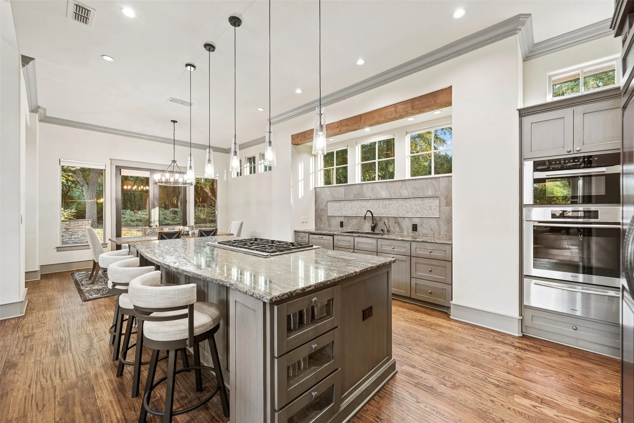 The central island features an integrated commercial-grade gas cooktop, abundant pull-out drawers, and specialty glass display cabinetry.