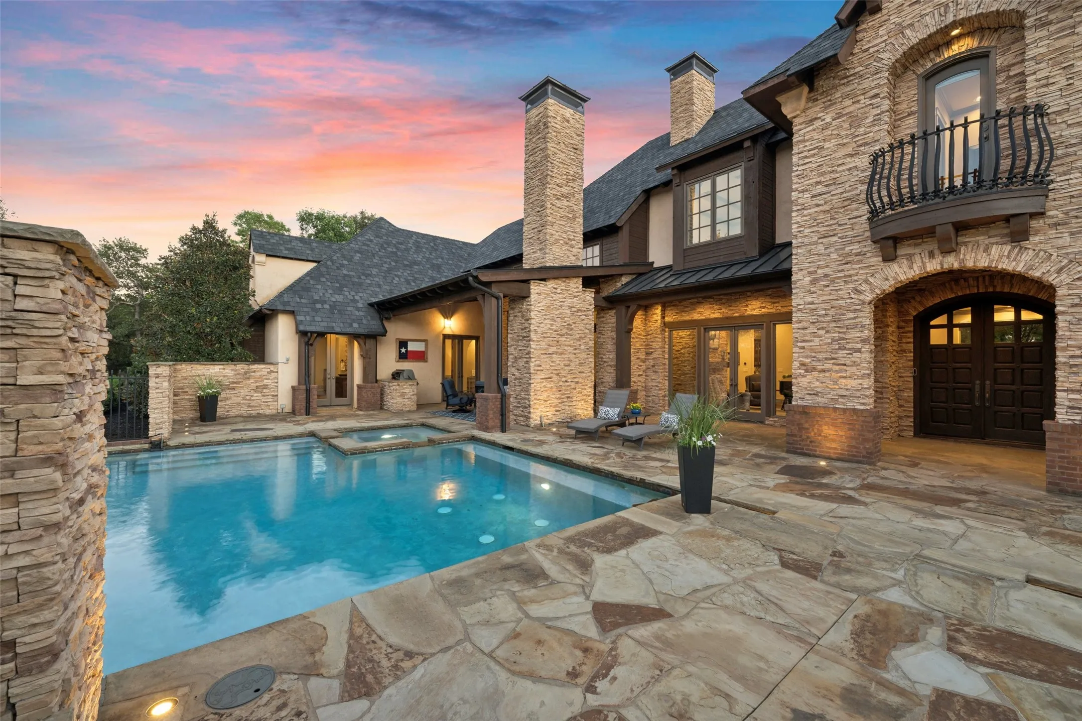 Expansive flagstone decking surrounds the private courtyard, accented by dramatic stacked-stone columns, integrated landscape lighting, and classic Mediterranean architecture